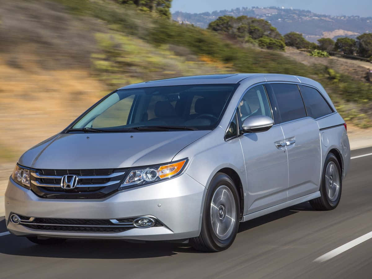 Honda Odyssey 桌布 壁紙 — 一架銀色本田小型貨車在陽光普照的高速公路上飛馳，背景是模糊的綠色山丘。