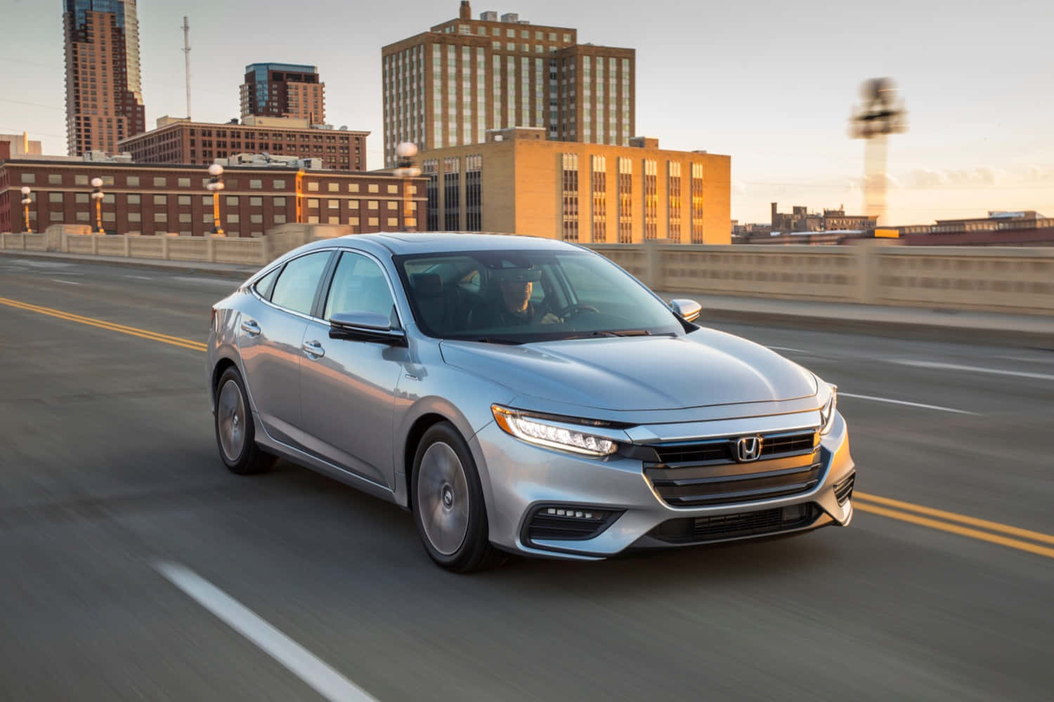 Honda Insight 桌布 壁紙 — 一架銀色本田房車在黃金時段行駛於城市橋樑上，背景是模糊的城市建築。