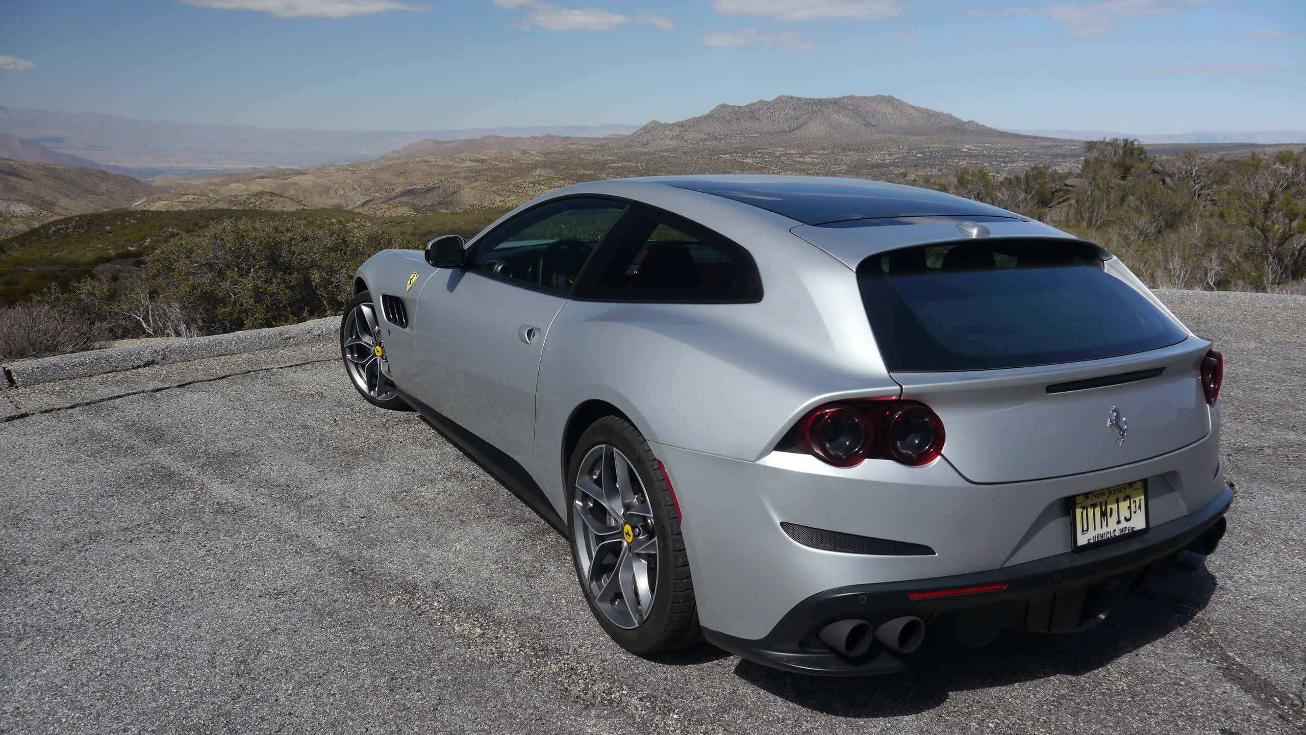 Ferrari Gtc4lusso 桌布 壁紙 — 一架銀色法拉利 GTC4Lusso 停泊在碎石觀景點，俯瞰乾旱山丘和遠山，天空清澈湛藍。