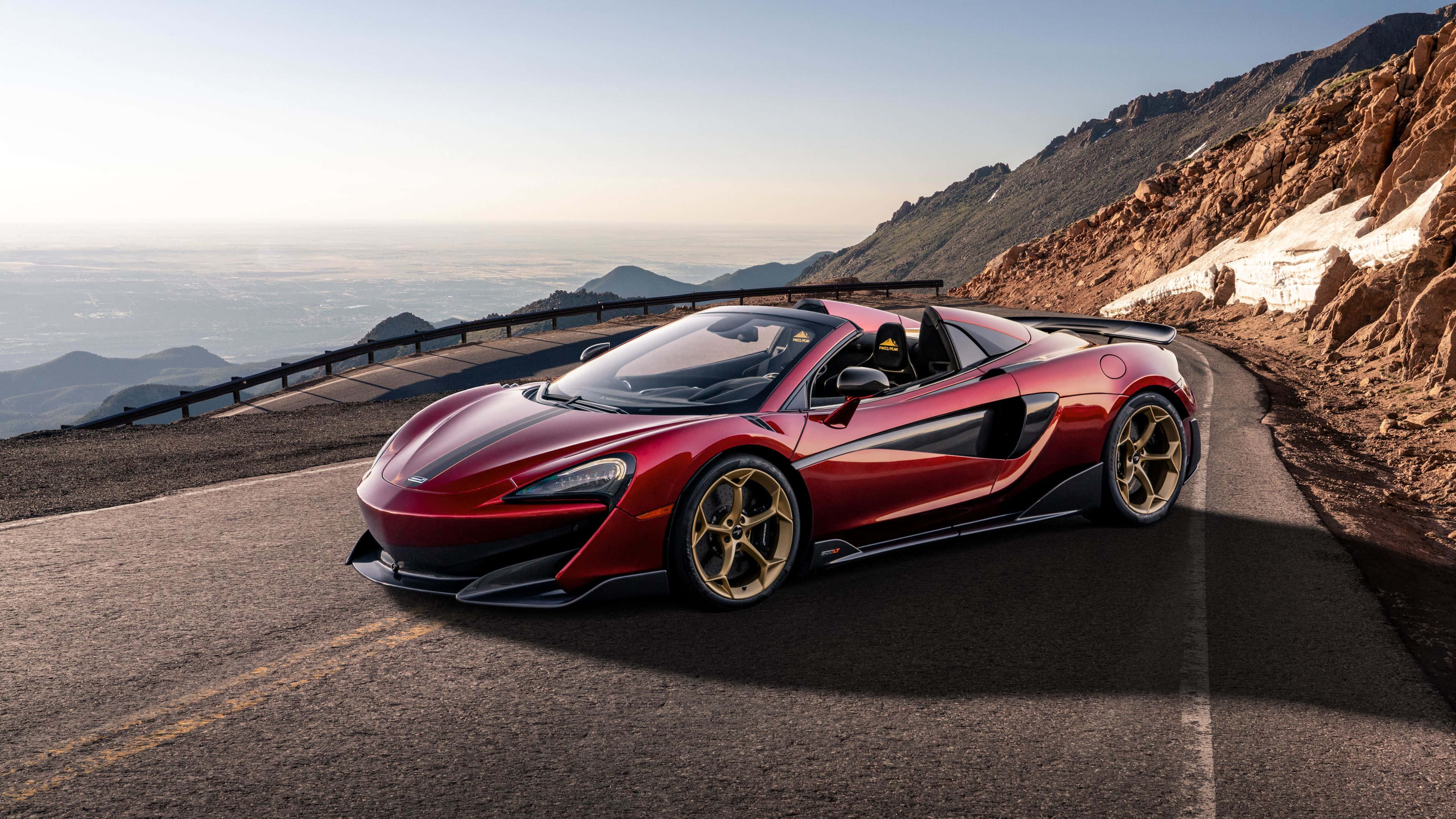 Mclaren 600lt 桌布 壁紙 — 一架閃亮紅色McLaren跑車配金色輪圈，在日出時分沿著蜿蜒山路行駛，俯瞰廣闊山谷。