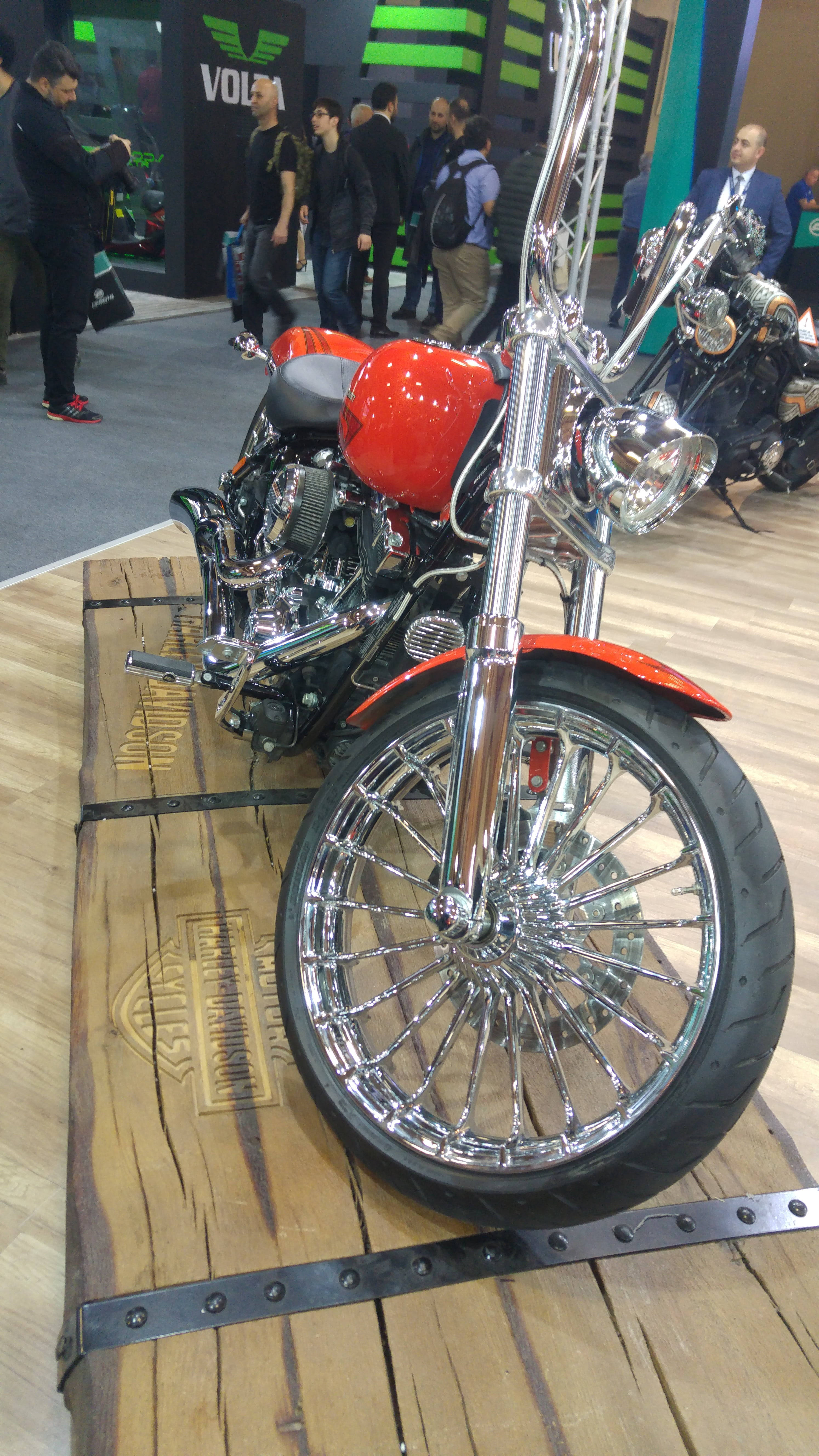 哈雷戴維森 桌布 壁紙 — 一架閃亮紅色和鍍鉻的Harley-Davidson電單車在擁擠的展覽廳的木製平台上展示。