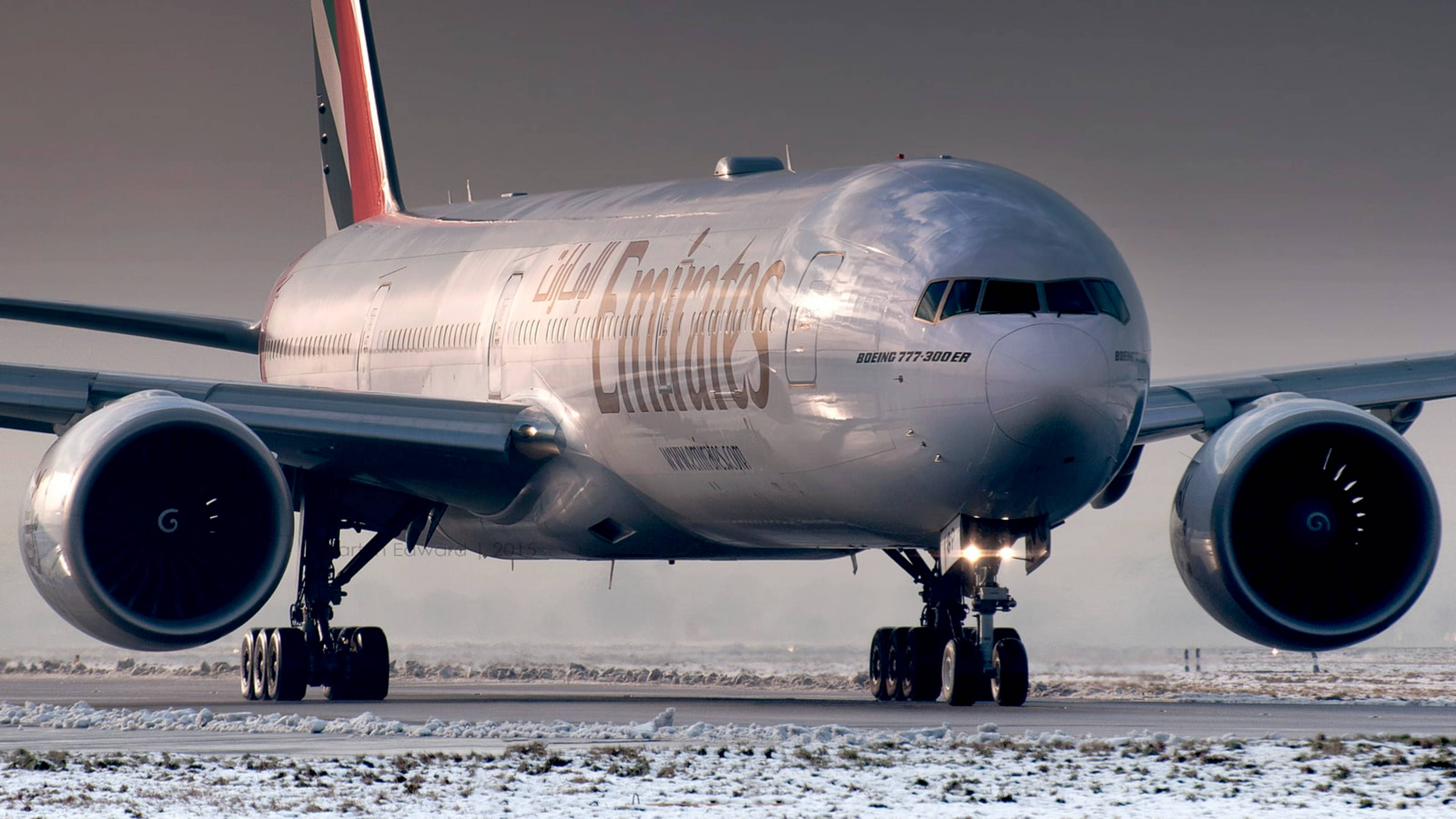 飛機 桌布 壁紙 — 一架阿聯酋航空波音777-300ER飛機在灰色天空下於積雪跑道滑行。