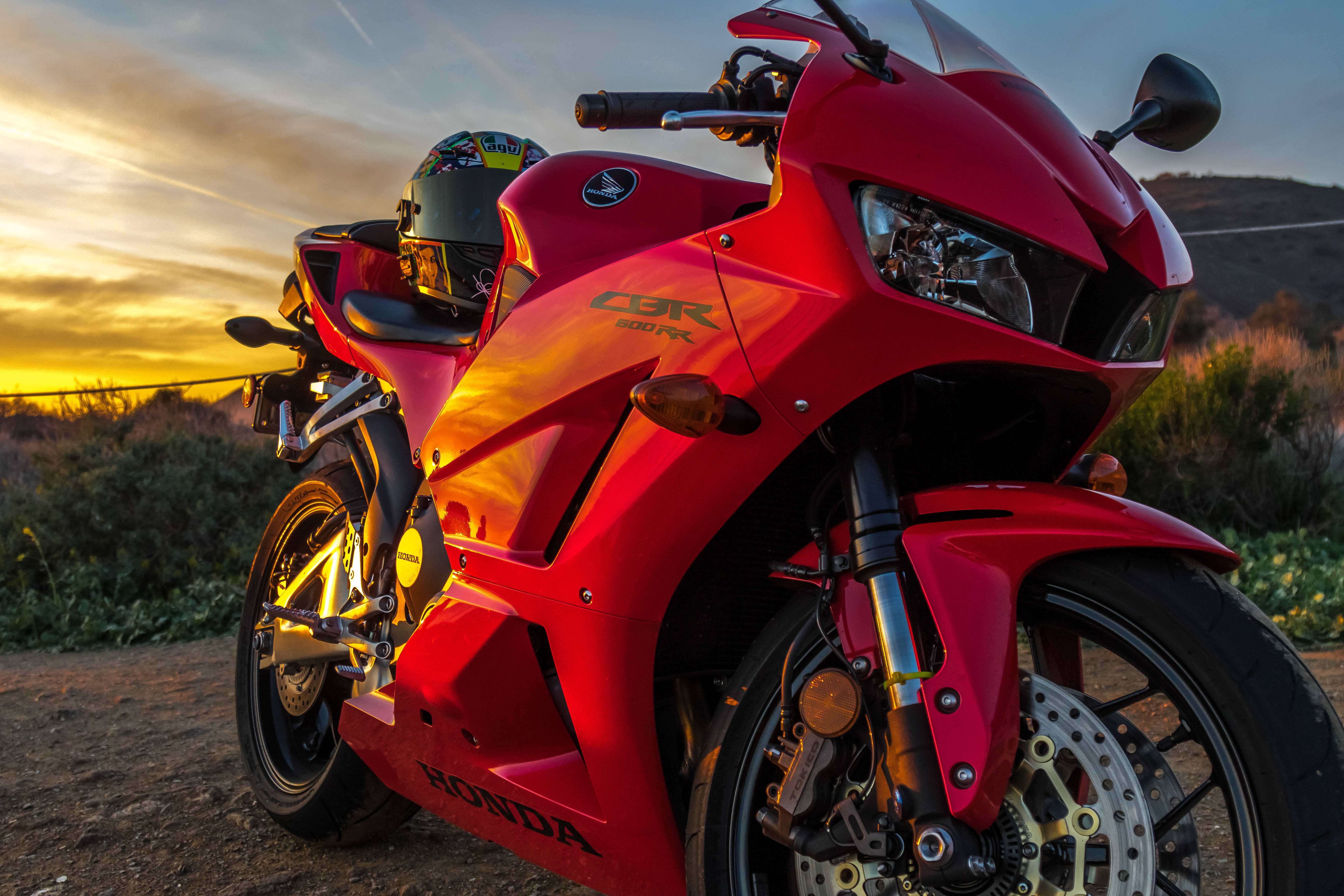 本田 桌布 壁紙 — 一架鮮紅色嘅Honda CBR 600 RR跑車喺金色夕陽下閃閃發光，停泊喺一條泥路上，背景係山丘。
