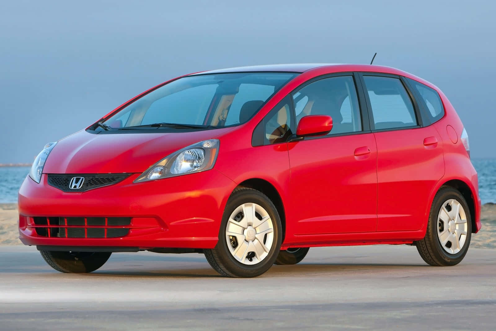 Honda Fit 桌布 壁紙 — 一架鮮紅色嘅Honda Fit停泊喺沙灘上，背景係海浪同柔和嘅藍天。