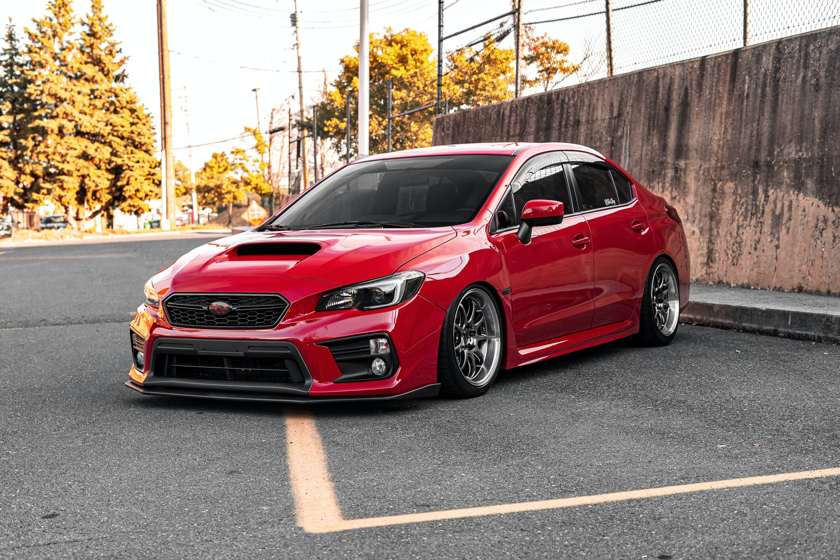 Sports Car 桌布 壁紙 — 一架鮮紅色嘅Subaru WRX STI泊喺瀝青路上，背景有秋天嘅樹同埋一幅石屎牆。