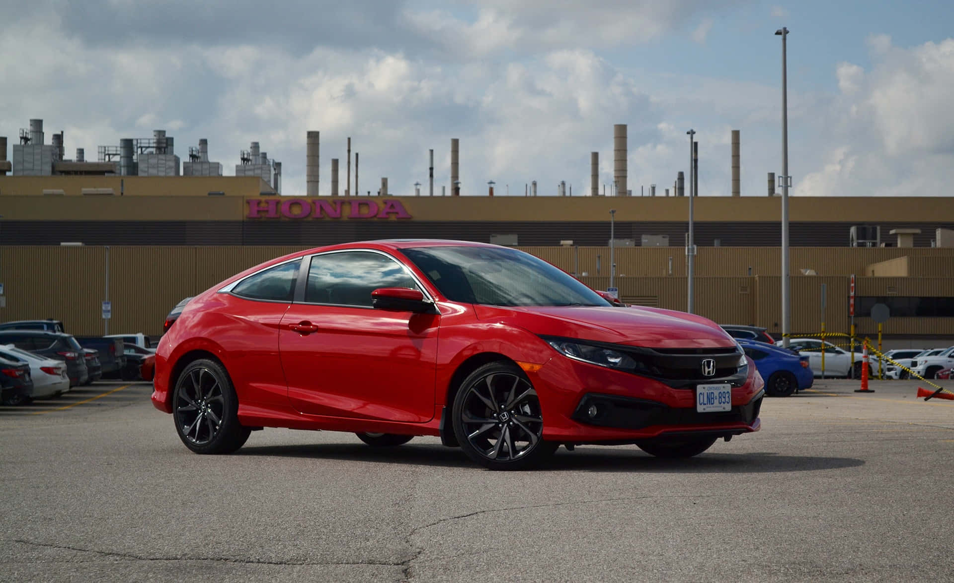 Honda Civic 桌布 壁紙 — 一架鮮紅色嘅本田思域轎跑車停喺停車場，背景係工廠同多雲嘅天空。