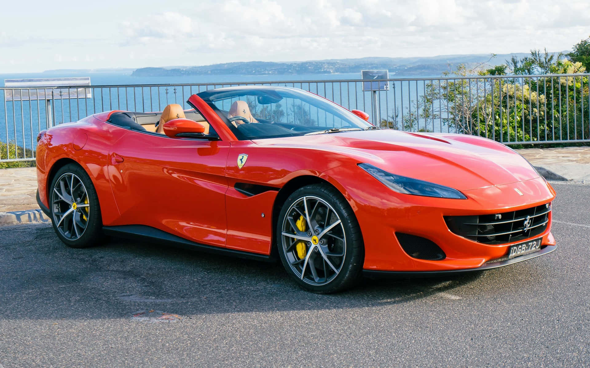Ferrari Portofino 桌布 壁紙 — 一架鮮紅色法拉利Portofino開篷跑車停泊在海邊觀景點，可欣賞海景，車內有兩人。