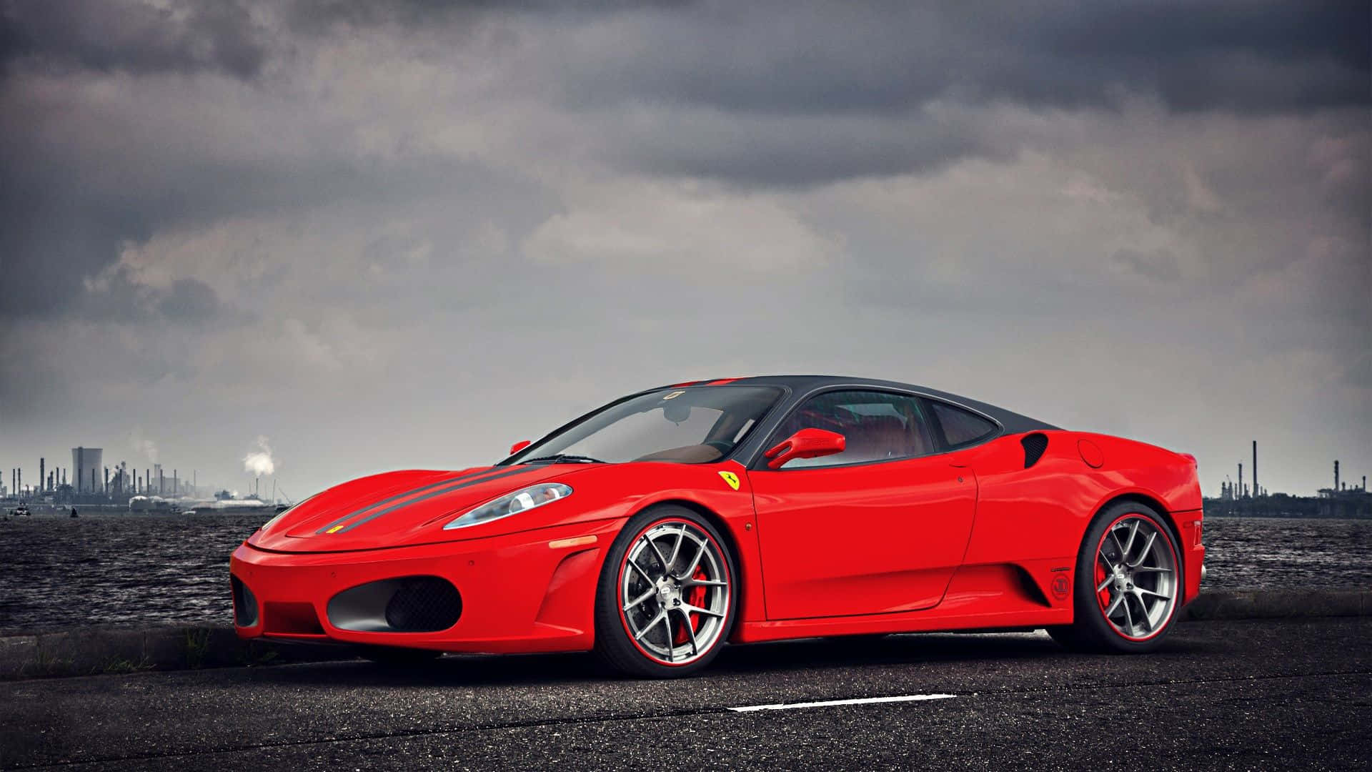 Ferrari F430 桌布 壁紙 — 一架鮮紅色法拉利跑車停在瀝青路上，背景是戲劇性的多雲天空和遠處的工業建築。