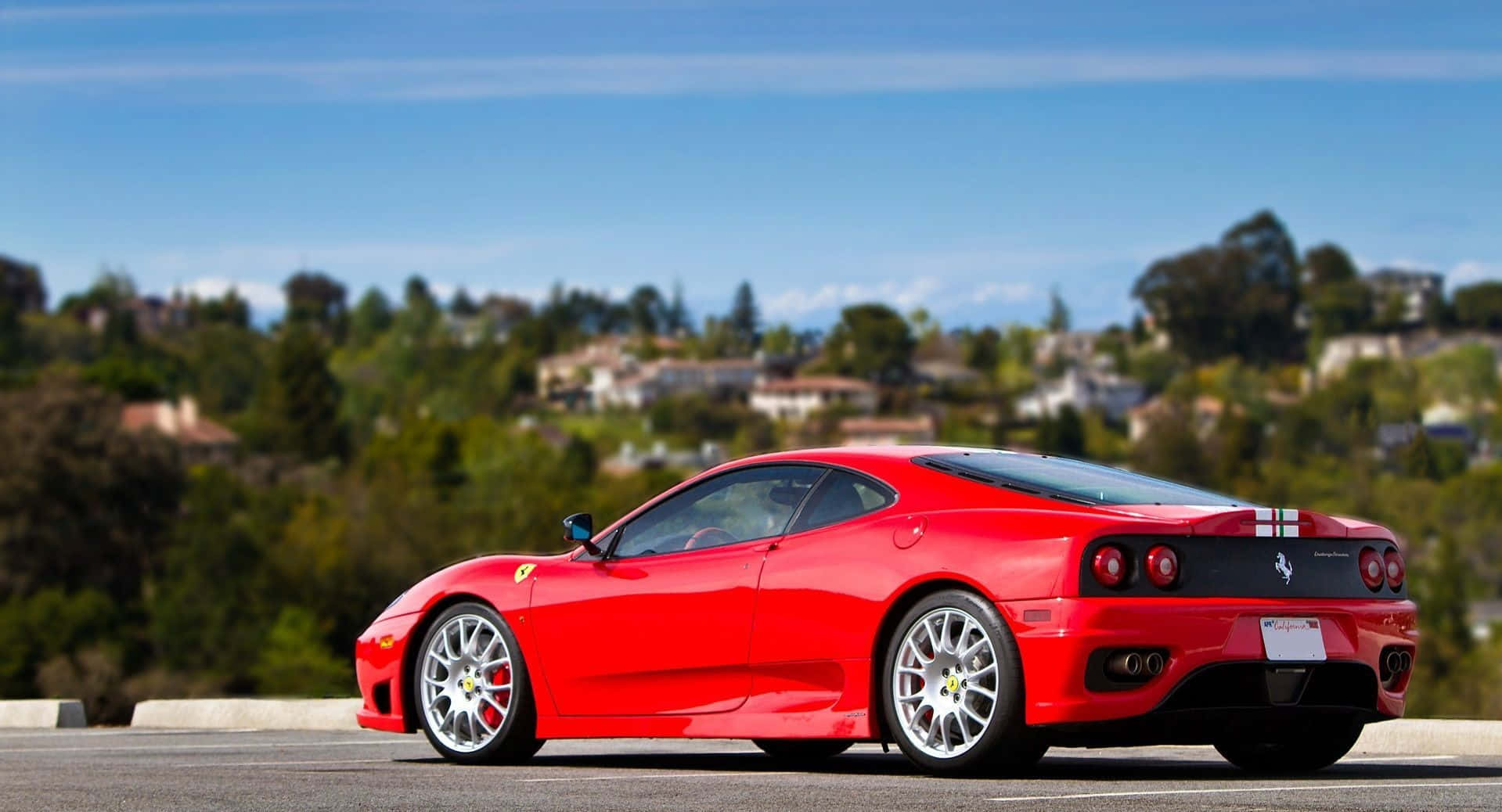 Ferrari 360 Modena 桌布 壁紙 — 一架鮮紅色法拉利跑車停泊在陽光明媚的高速公路上，俯瞰著綠草如茵、房屋林立的丘陵。
