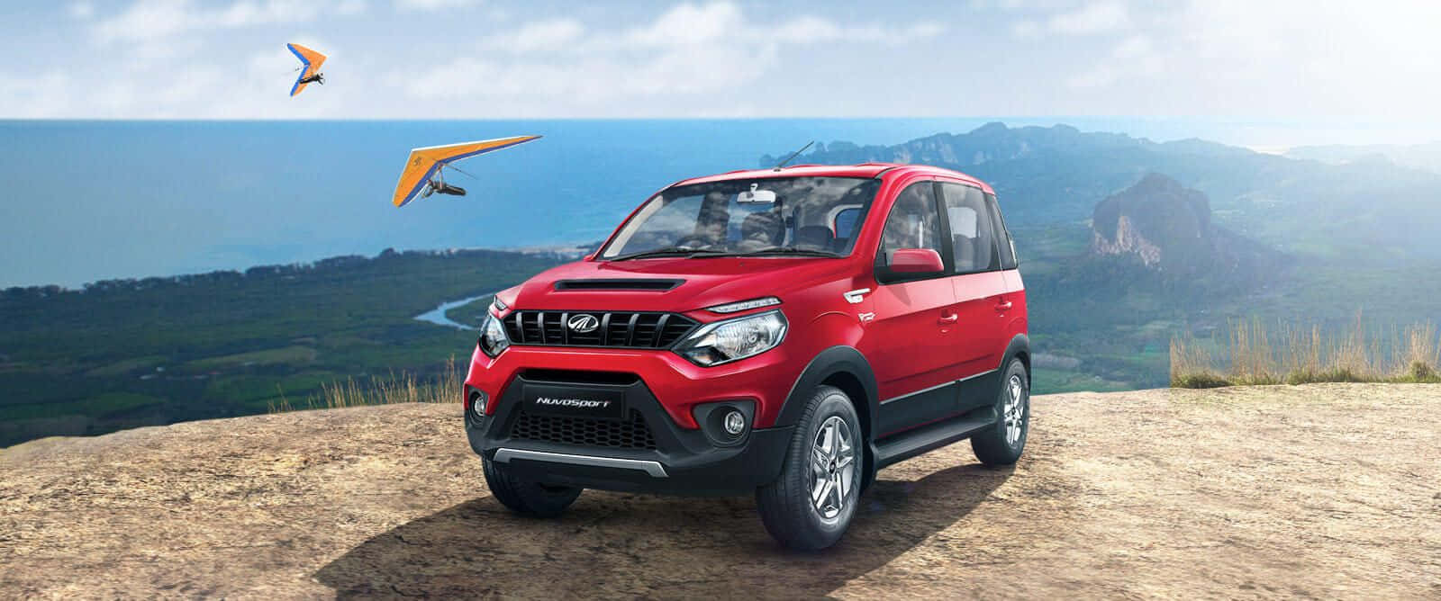 Mahindra 桌布 壁紙 — 一架鮮紅色的Mahindra TUV300 SUV停喺懸崖上，俯瞰海岸山谷，有兩個滑翔傘喺天空翱翔。