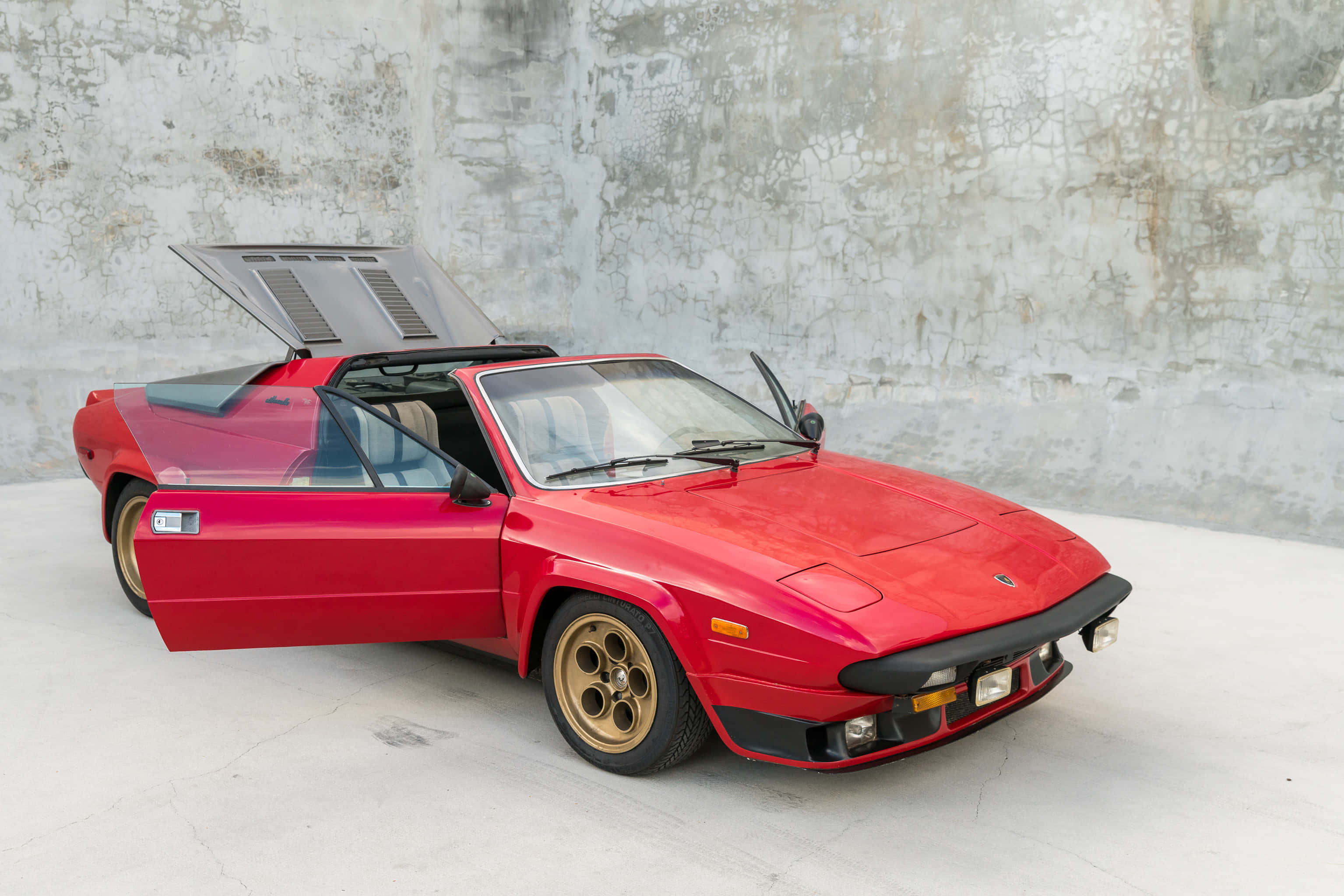 Lamborghini Silhouette 桌布 壁紙 — 一架鮮紅色經典跑車，鷗翼車門打開，停喺風化嘅混凝土牆前面。