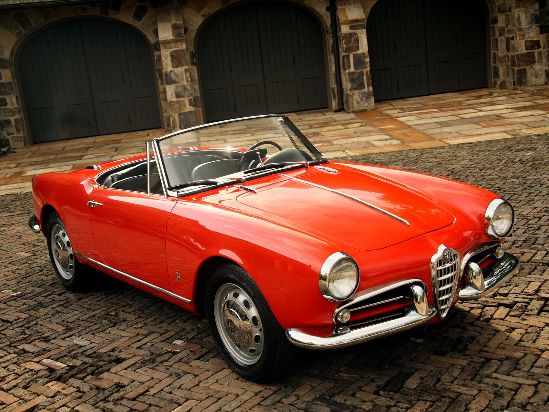Alfa Romeo Spider 桌布 壁紙 — 一架鮮紅色經典阿爾法羅密歐Spider開篷車停泊在石拱門前的鵝卵石庭院。