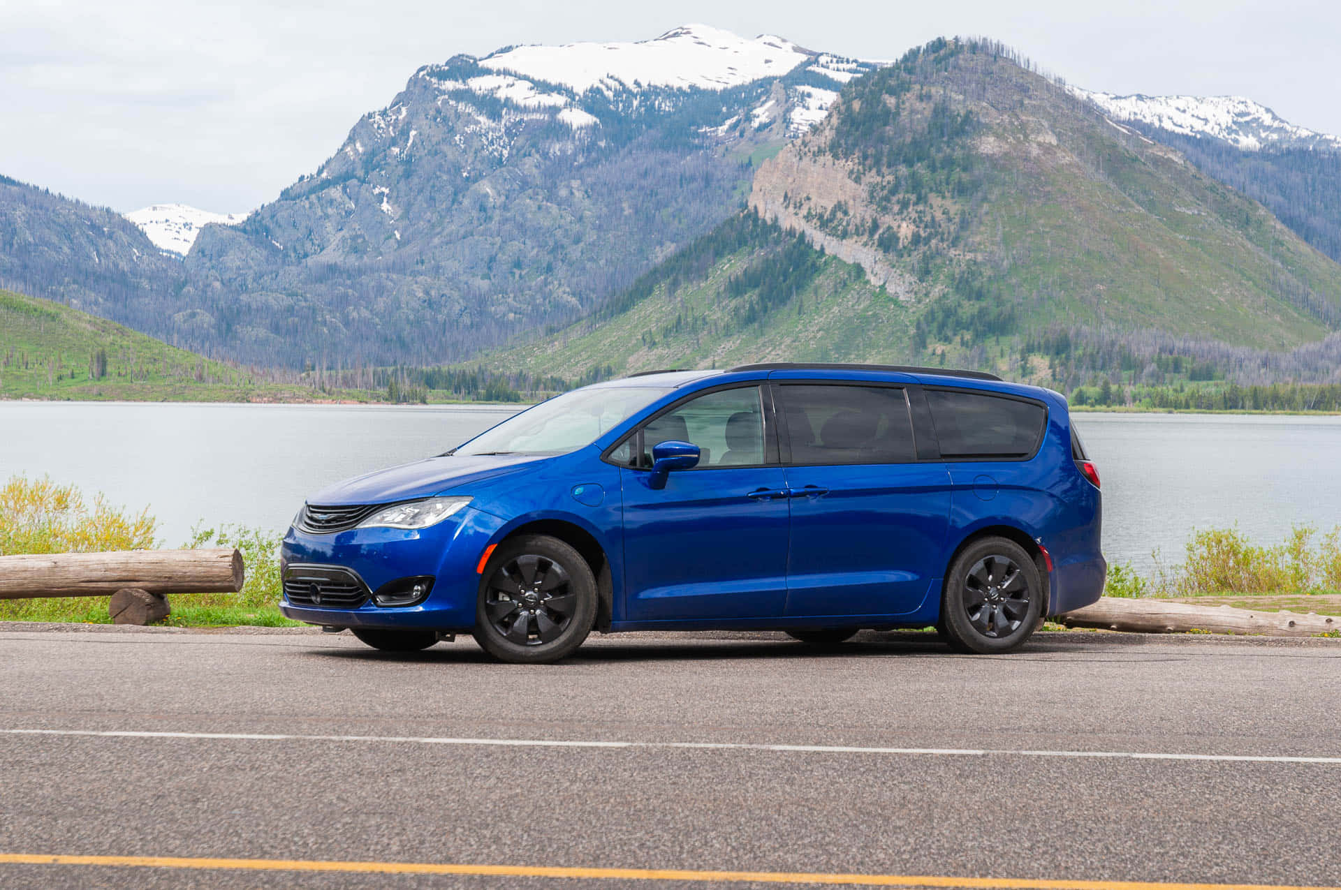 Chrysler Pacifica 桌布 壁紙 — 一架鮮藍色小型貨車停泊在湖邊，背後有積雪的山峰在陰天中聳立。