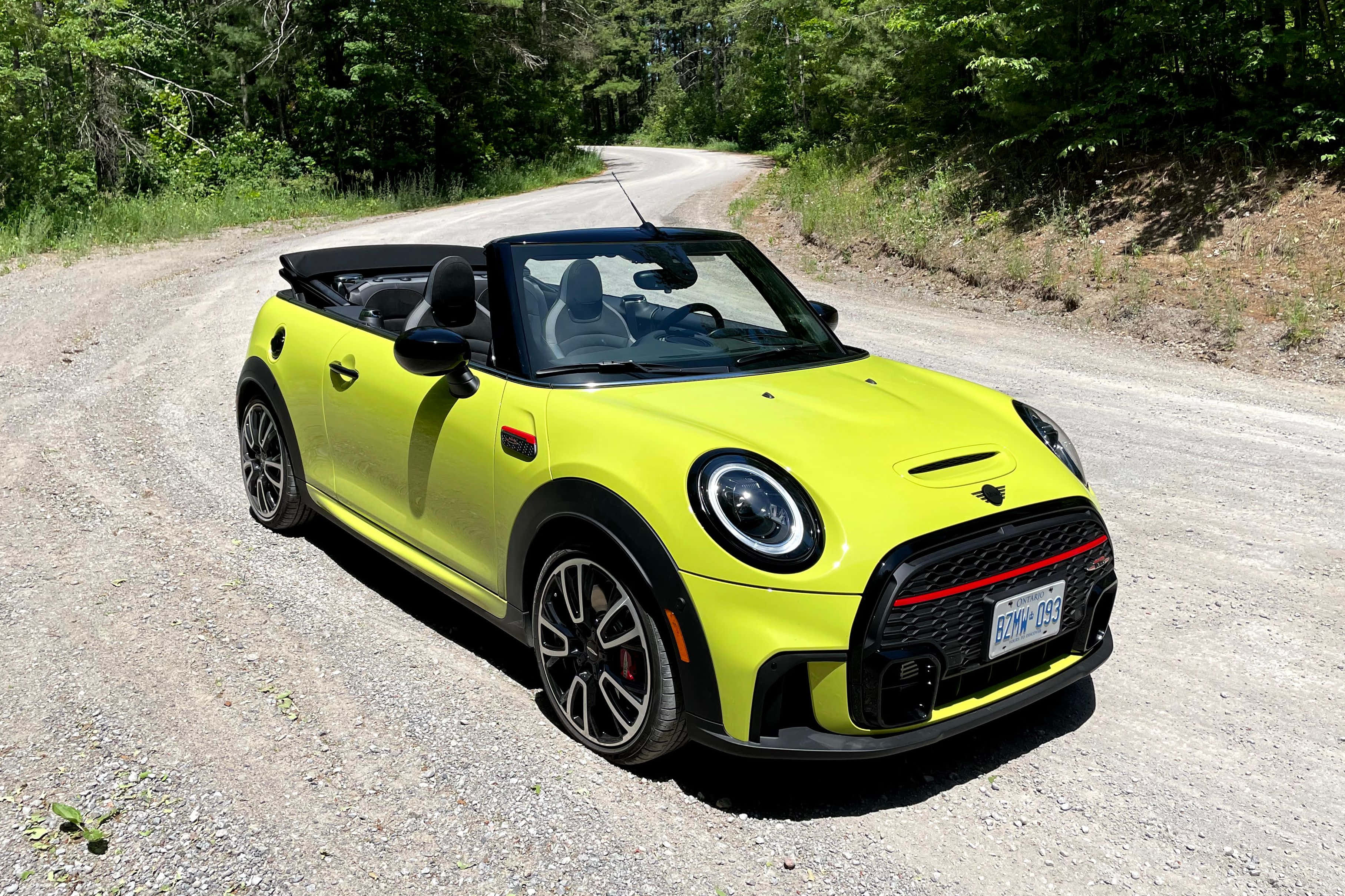 Mini Cooper Convertible 桌布 壁紙 — 一架鮮黃色嘅MINI Cooper開篷車停泊喺陽光普照嘅碎石路上，周圍係茂密嘅綠樹。