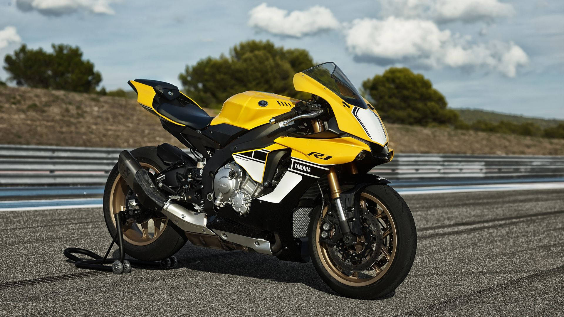 機車 桌布 壁紙 — 一架鮮黃色嘅Yamaha R1電單車停泊喺有護欄同綠色山丘嘅賽道上，天空局部多雲。