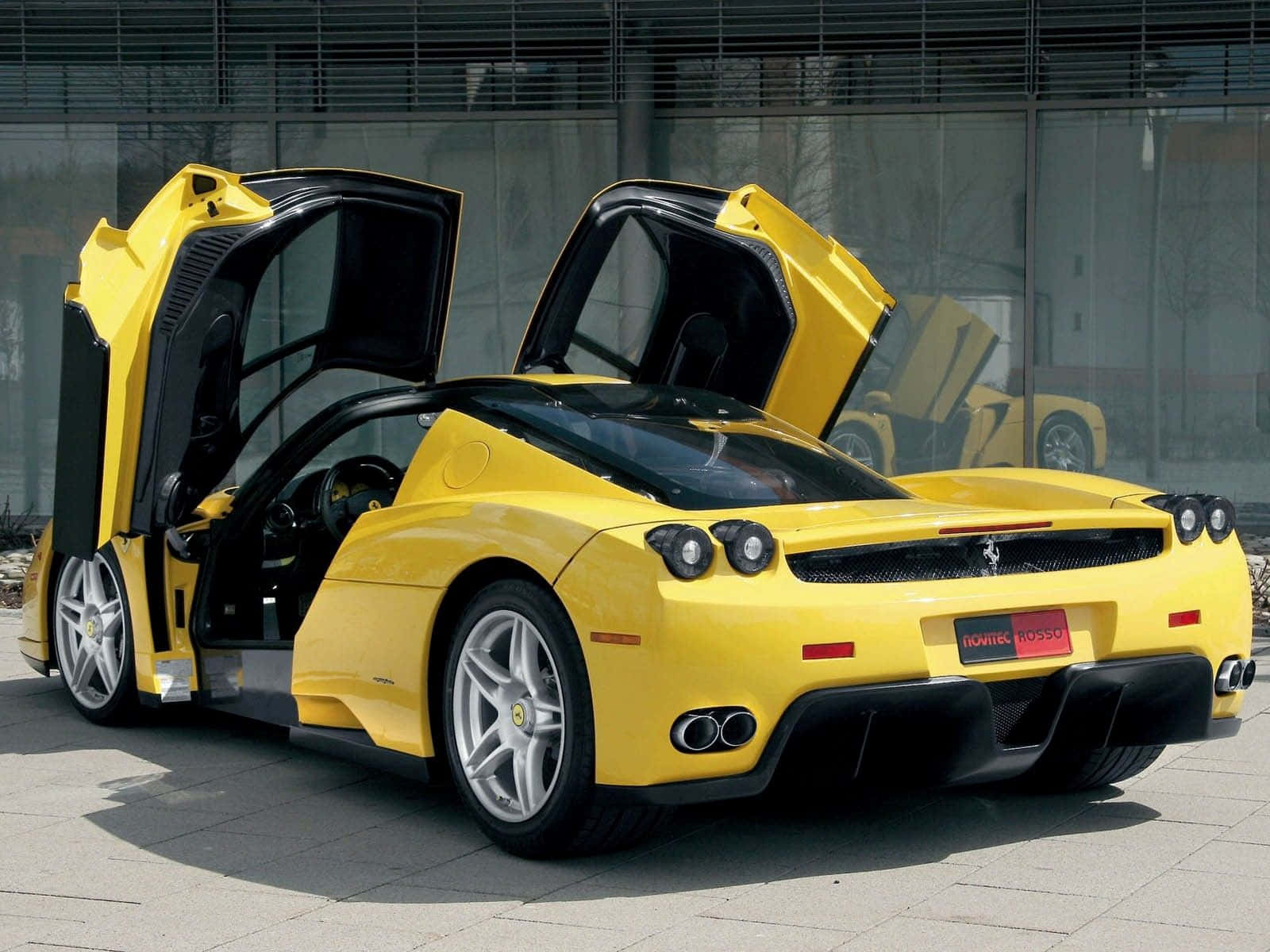 Yellow Car 桌布 壁紙 — 一架鮮黃色法拉利Enzo，剪刀門打開，停泊在現代玻璃建築前的鋪砌地面上。