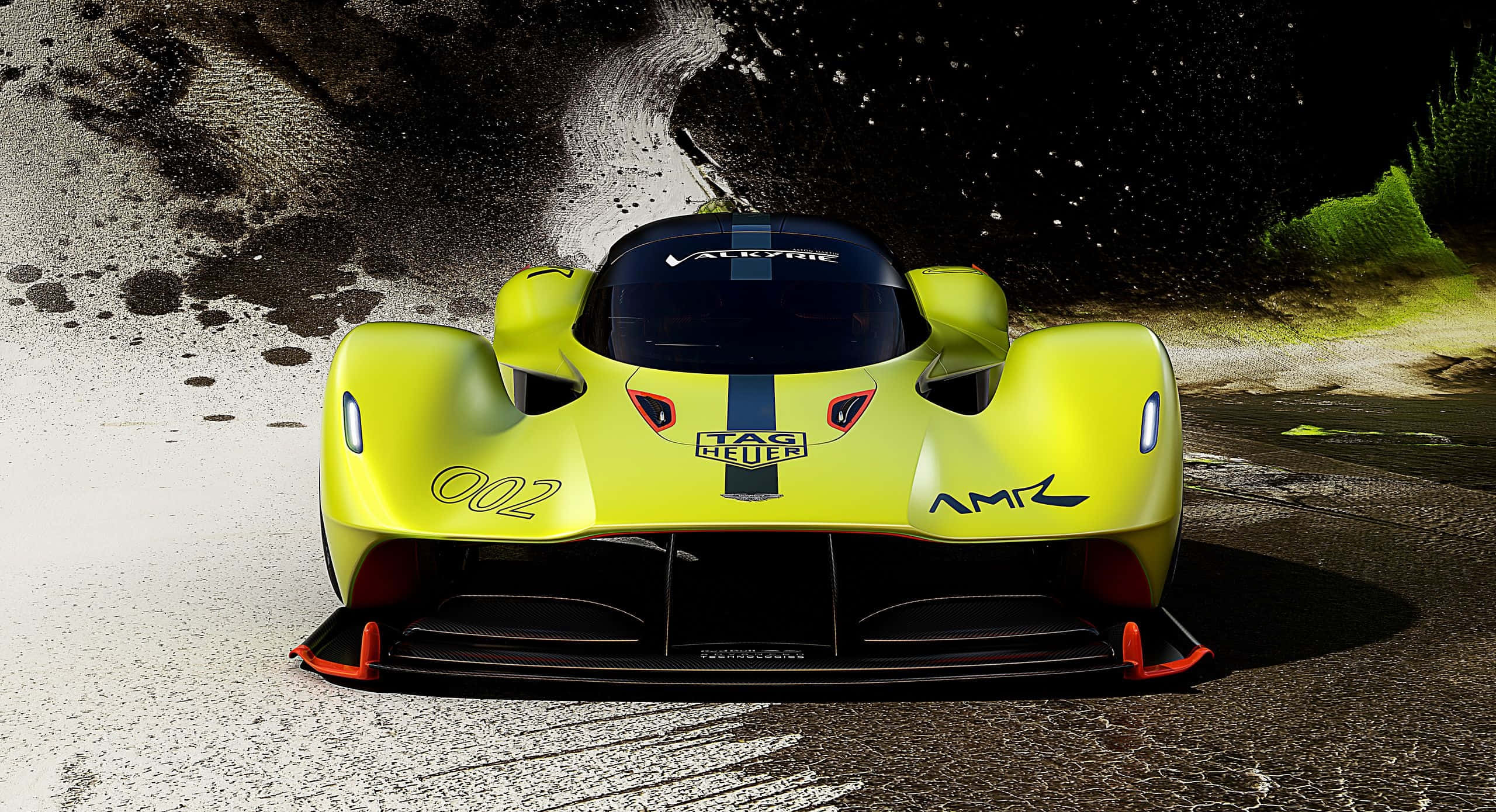 Aston Martin Valkyrie 桌布 壁紙 — 一架鮮黃色的Aston Martin AMR1賽車在潮濕的賽道上飛馳，濺起戲劇性的水花，背景昏暗。