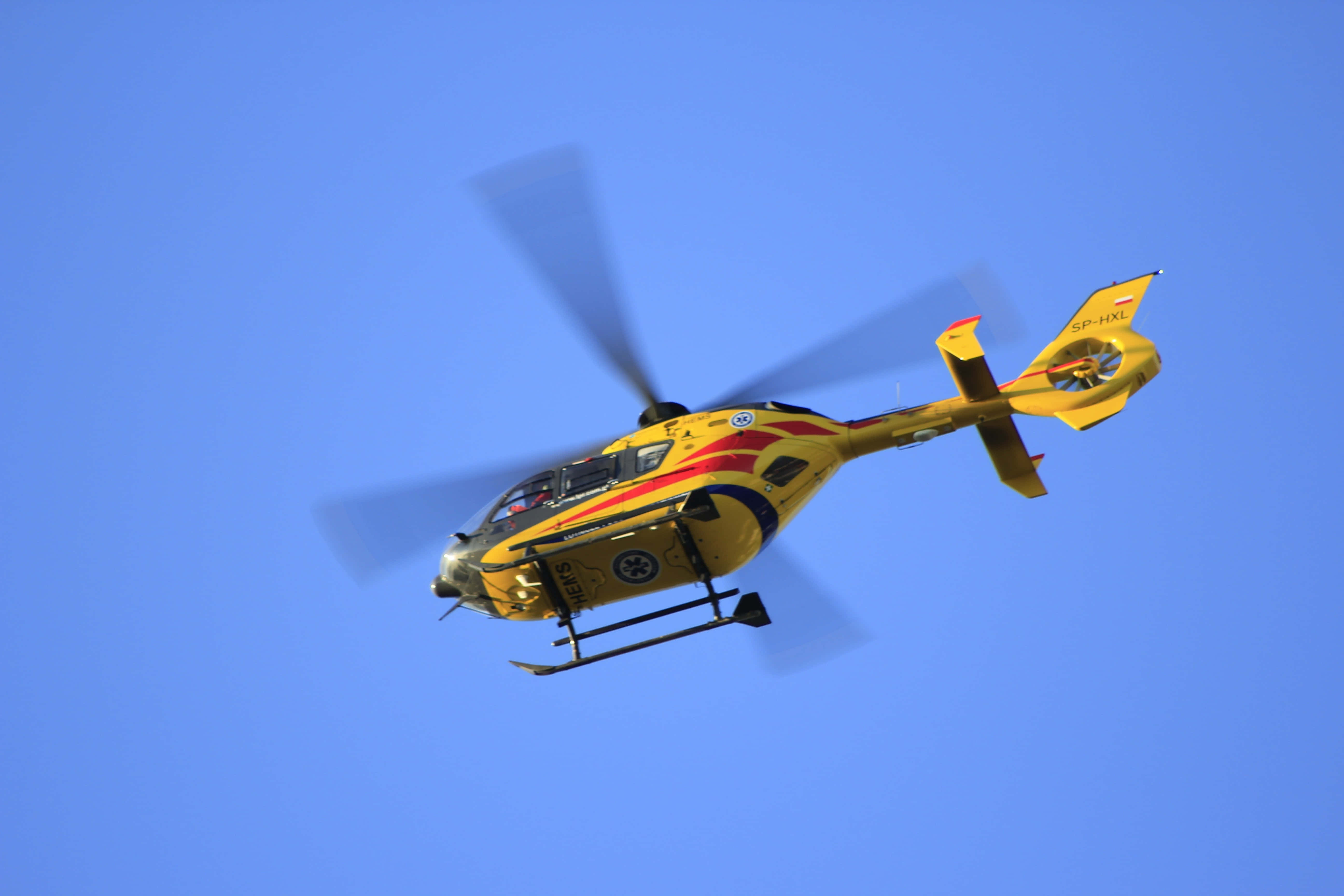 Helicopter 桌布 壁紙 — 一架黃色和紅色的救援直升機在晴朗的藍天中翱翔，旋翼轉動。