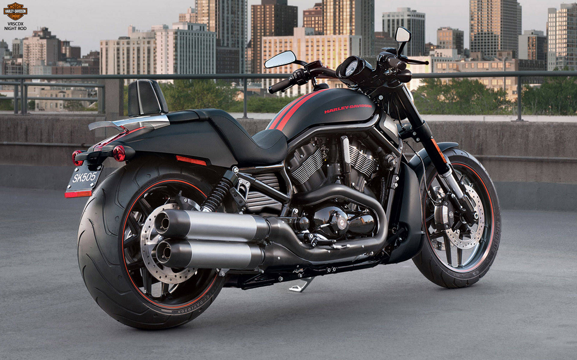 機車 桌布 壁紙 — 一架黑色Harley-Davidson Night Rod電單車帶有紅色點綴，停泊在可俯瞰天際線的城市屋頂上，正值黃昏。