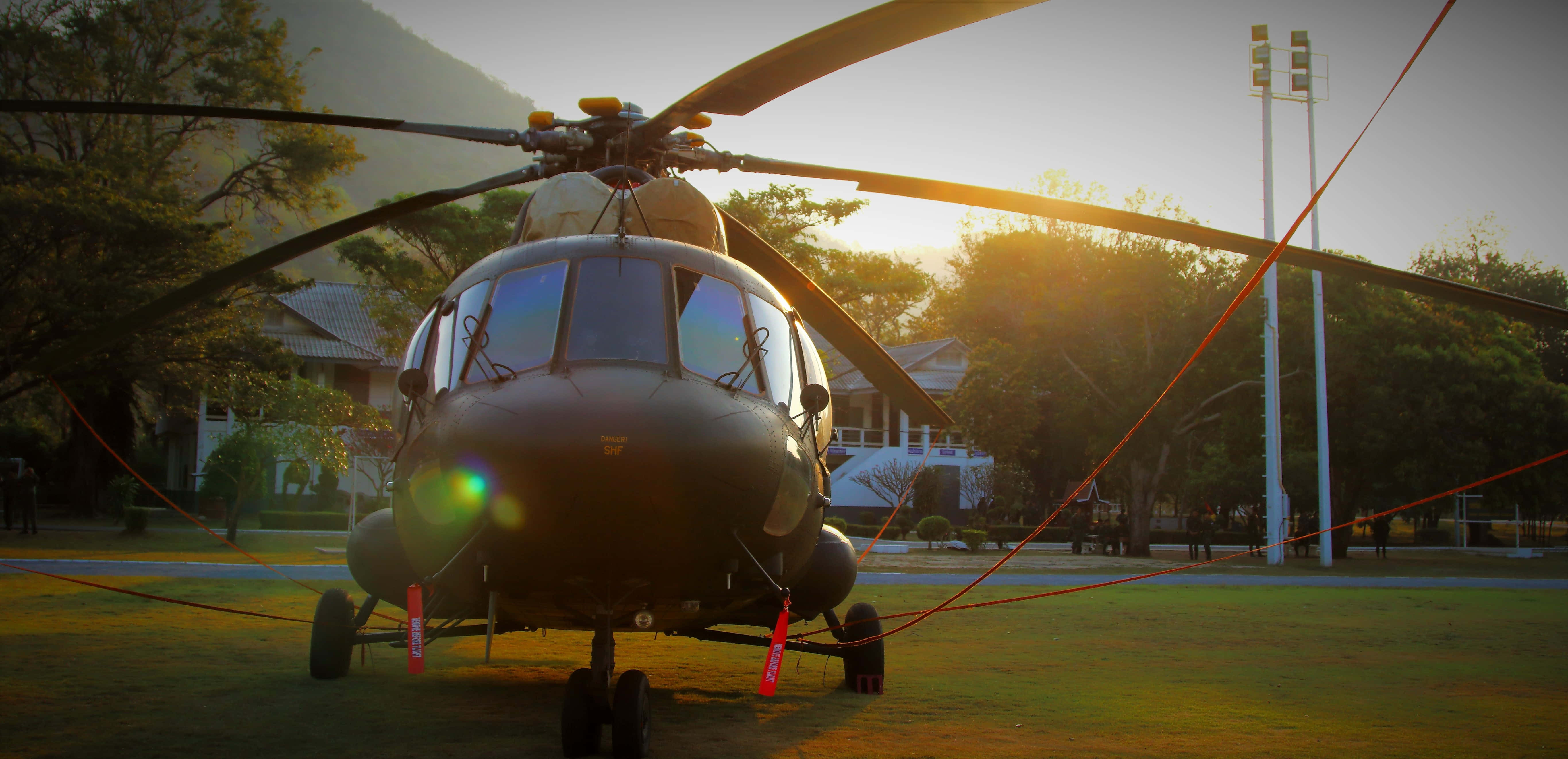 Helicopter 桌布 壁紙 — 一架黑色直升機在日落時分停在草地上，背景有樹木和體育場燈光。