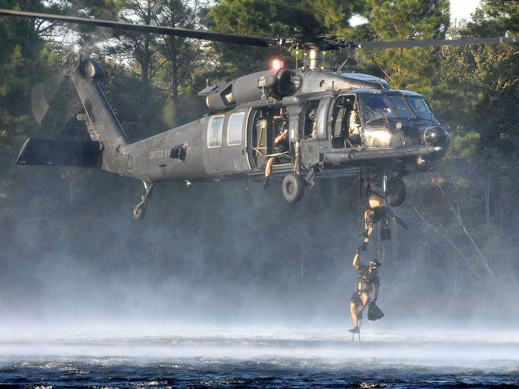 直升機 桌布 壁紙 — 一架黑色軍用直升機低空盤旋在水面上，一名士兵正沿繩索下降至霧氣瀰漫的水面。