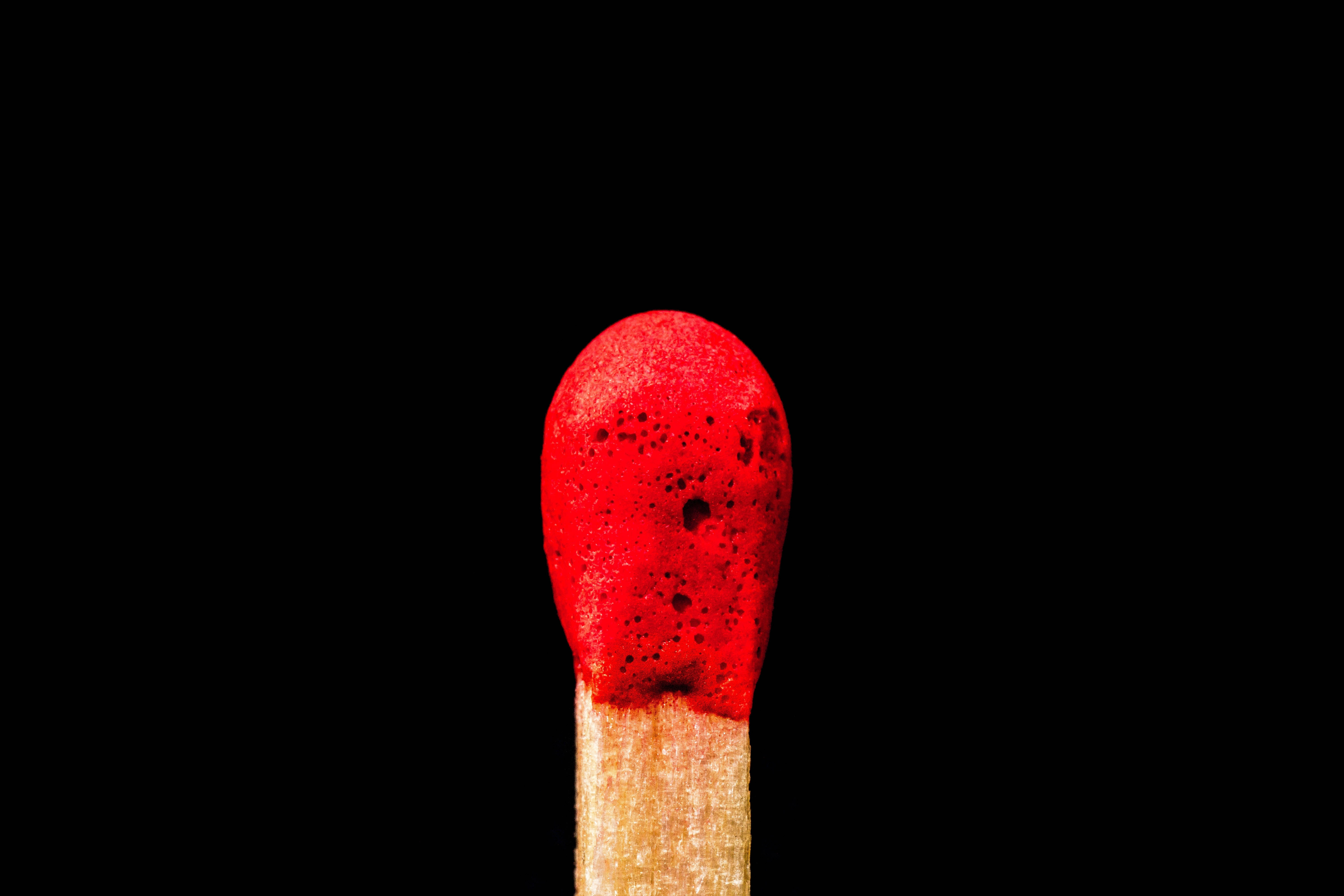 紅黑 桌布 壁紙 — 一根火柴，帶有紋理的紅色頭部，居中放置在純黑色背景上。