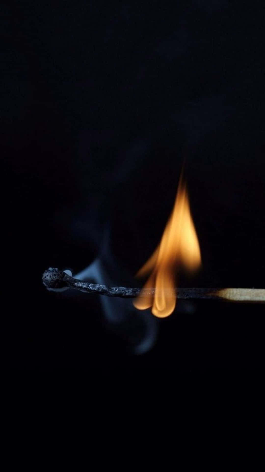 Burn 桌布 壁紙 — 一根點燃的火柴在深黑色背景上投射出溫暖的橙色火焰，縷縷煙霧升起。