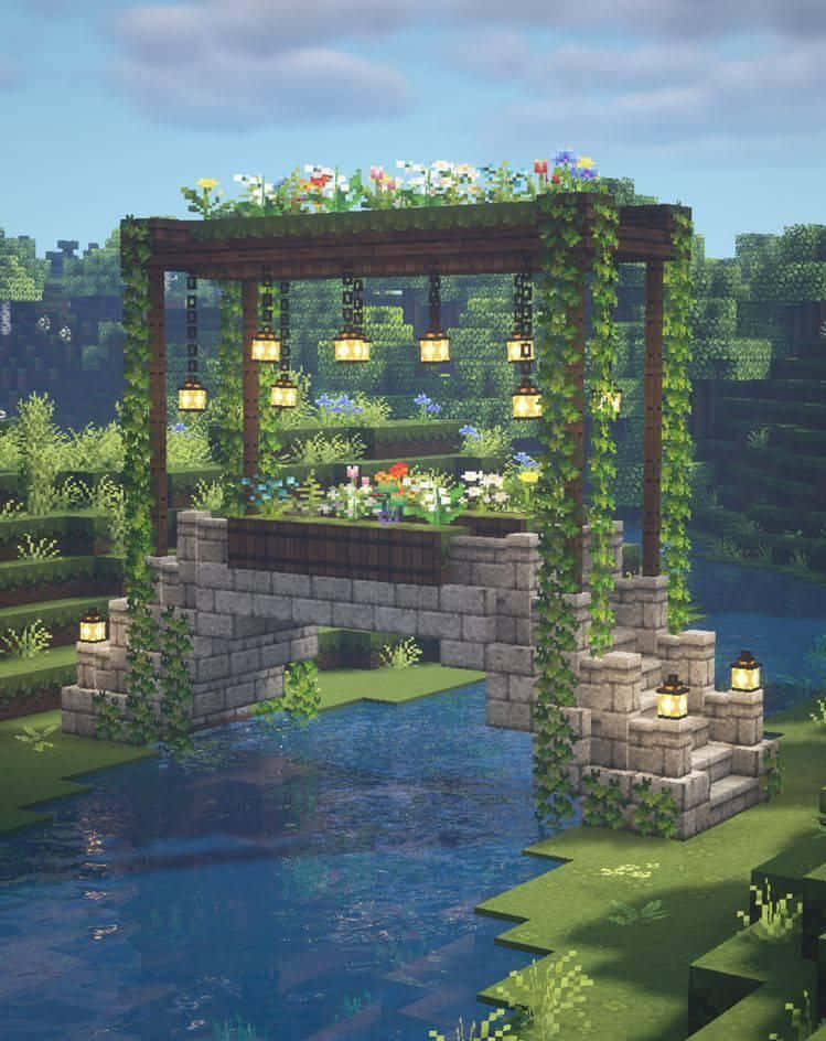 Minecraft Architecture 桌布 壁紙 — 一條像素化的石橋拱跨在平靜的河面上，上方是覆蓋著藤蔓和發光燈籠的木製涼棚。