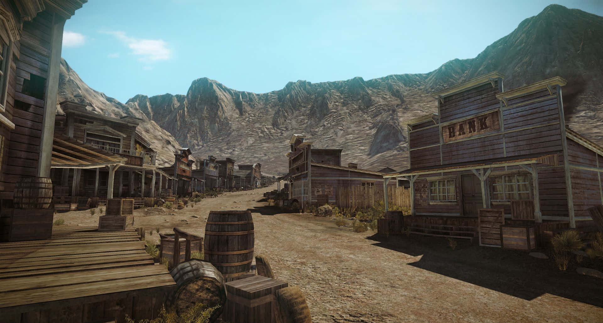 Wild West 桌布 壁紙 — 一條塵土飛揚的西部小鎮街道，兩旁是木造建築和木桶，背景是晴朗的藍天和岩石山脈。