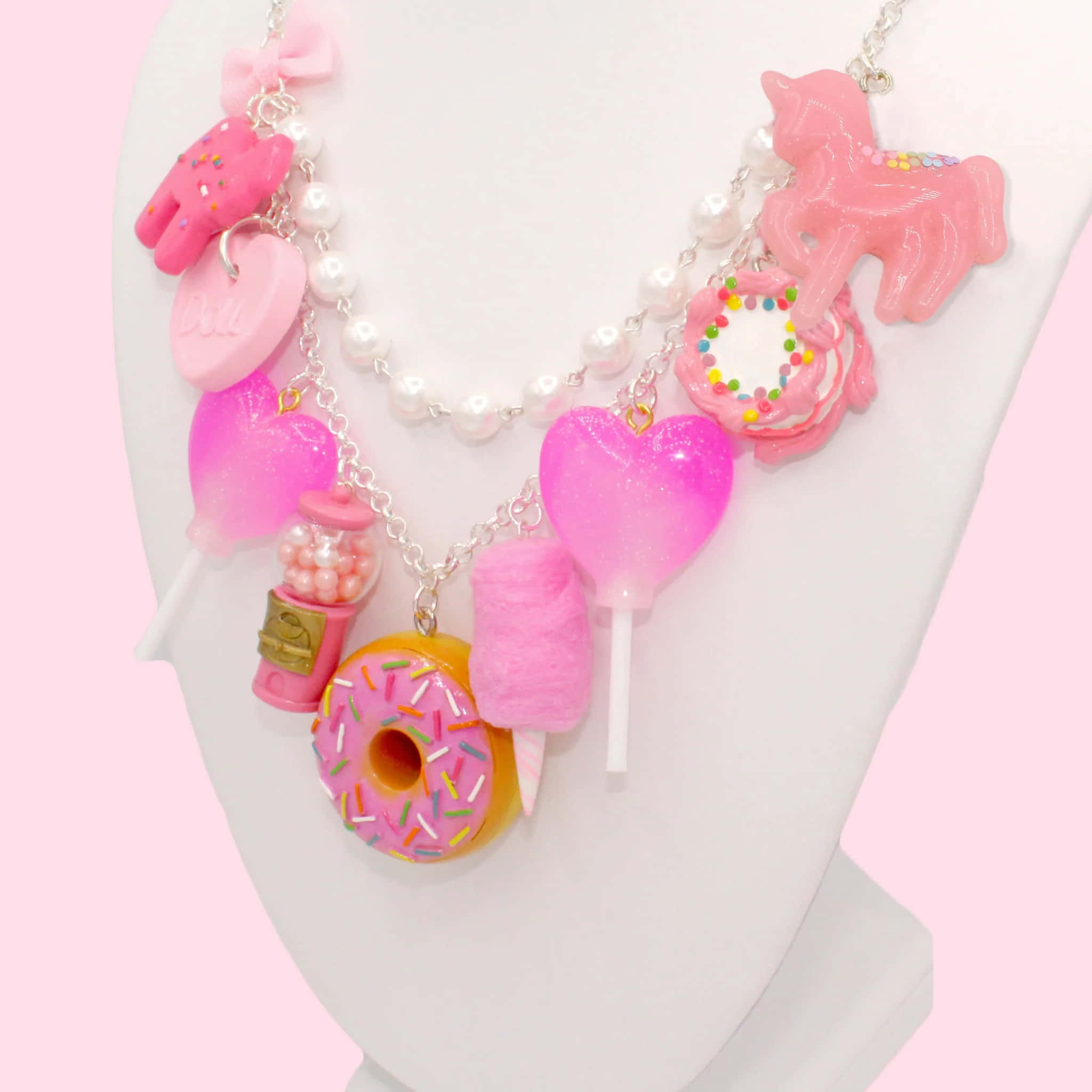 Pink Candy 桌布 壁紙 — 一條夢幻的粉紅色糖果主題項鍊，飾有冬甩、心形和獨角獸，展示在模特兒半身像上，背景是柔和的粉紅色。