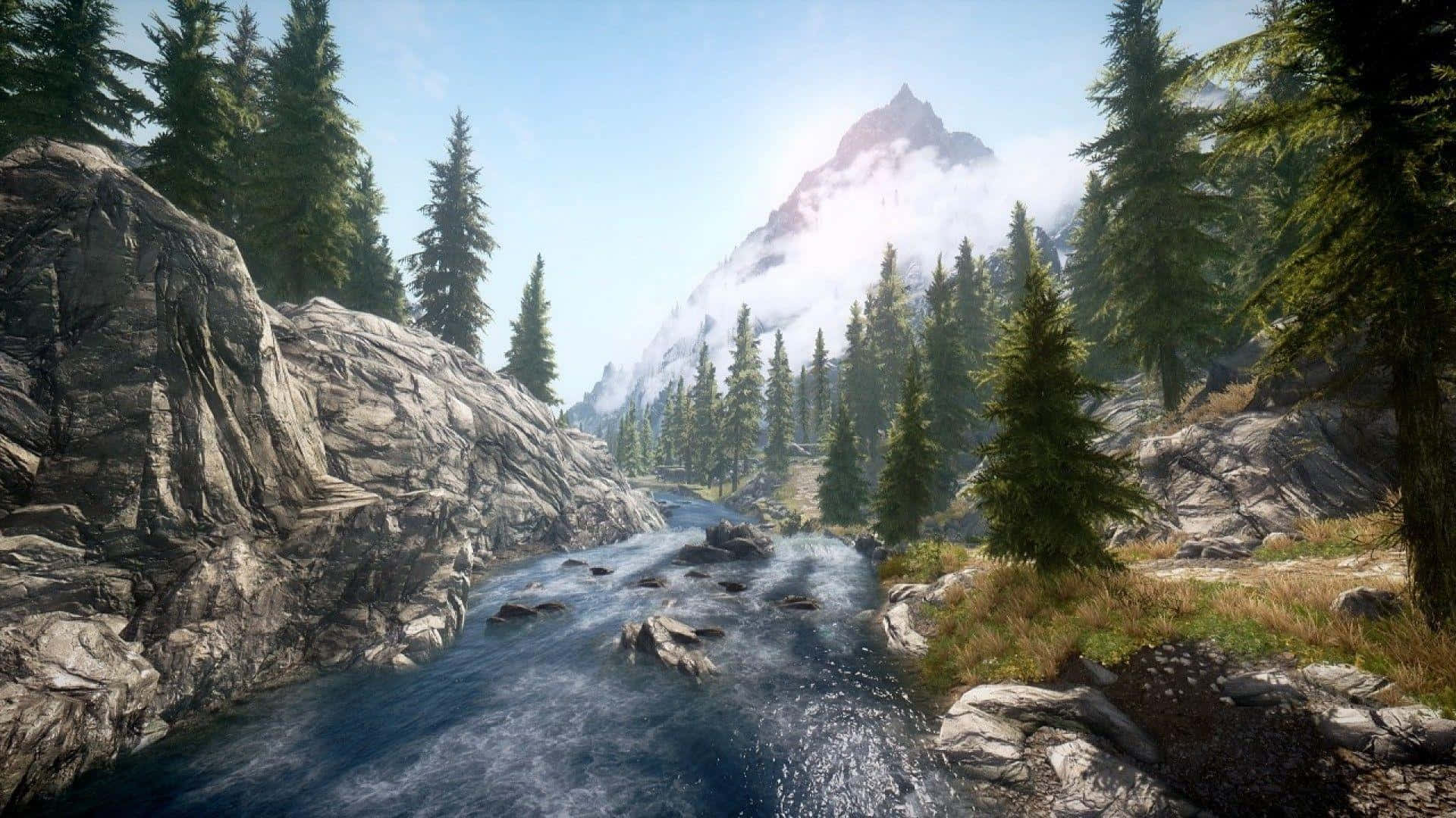 Skyrim Landscapes 桌布 壁紙 — 一條寧靜的山間溪流蜿蜒穿過岩石地形和茂密的松林，在明亮的天空下，遠處有一座積雪的山峰。