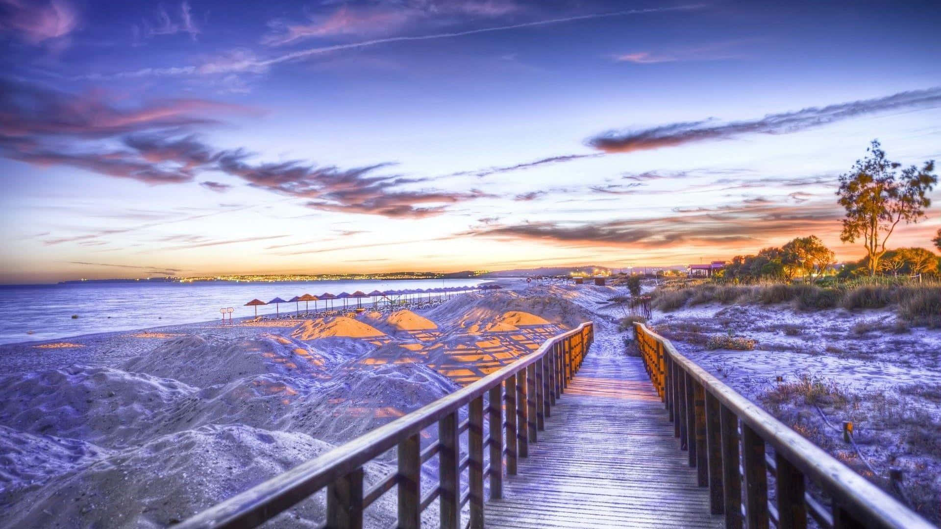 Beautiful Ocean 桌布 壁紙 — 一條木製步道在充滿活力的紫色、橙色和藍色天空下，通往日落時分的海灘。