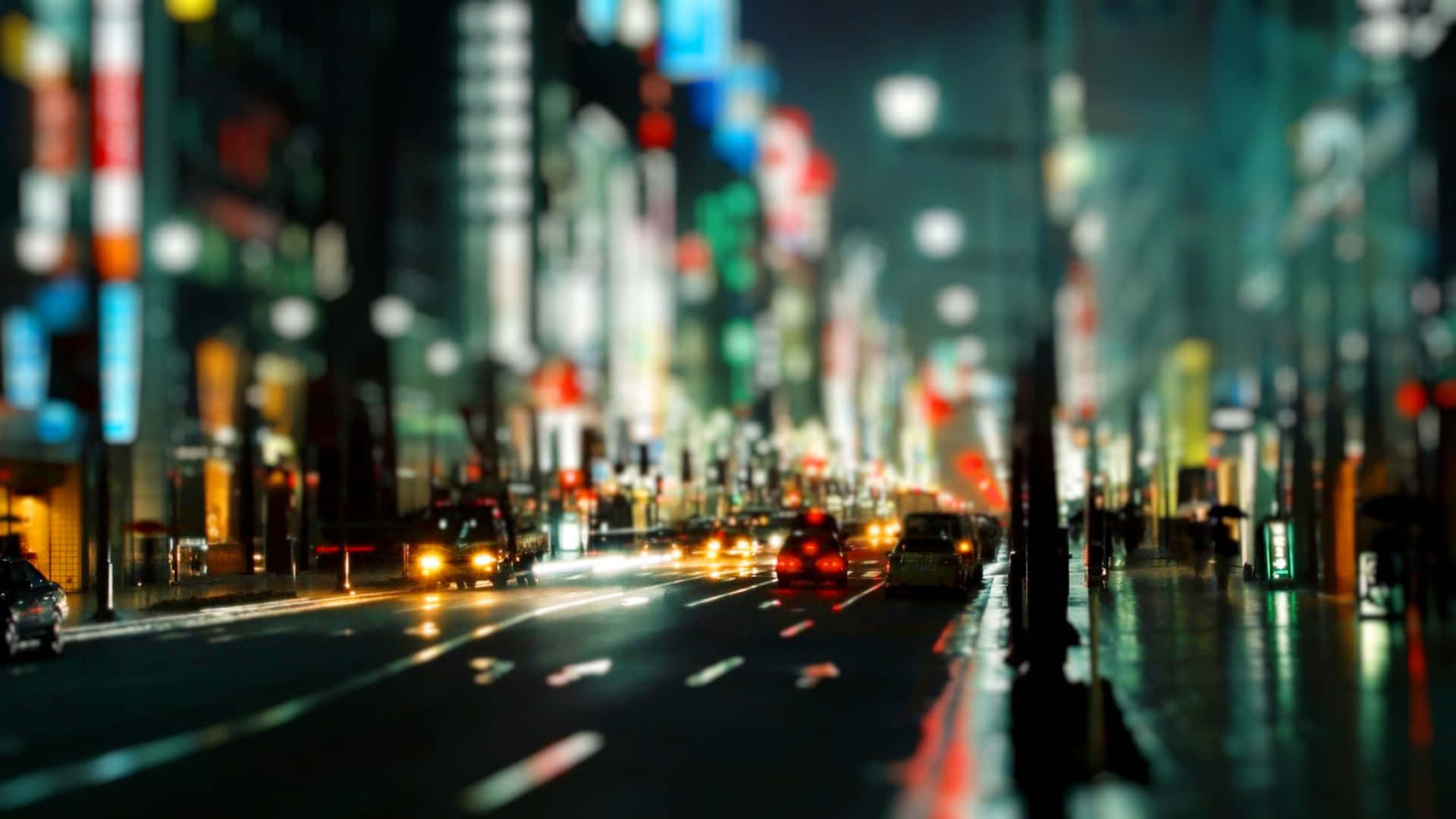 Night Street 桌布 壁紙 — 一條模糊的夜間城市街道，有發光的車燈和霓虹燈招牌在濕漉漉的人行道上反射。