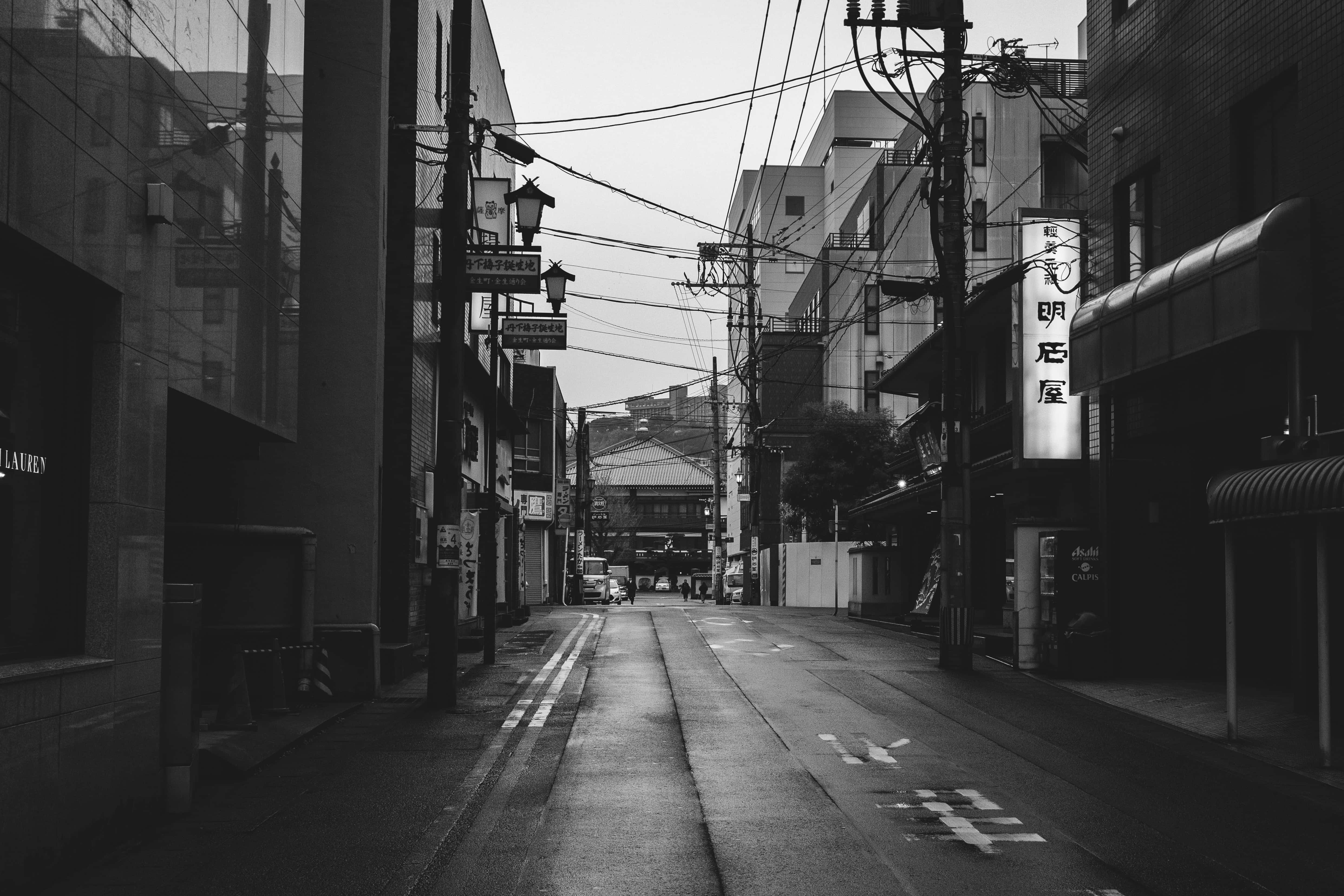 黑白美學 桌布 壁紙 — 一條狹窄城市小巷的黑白景觀，濕漉漉的路面反射出高樓之間架空電線和發光招牌的倒影。