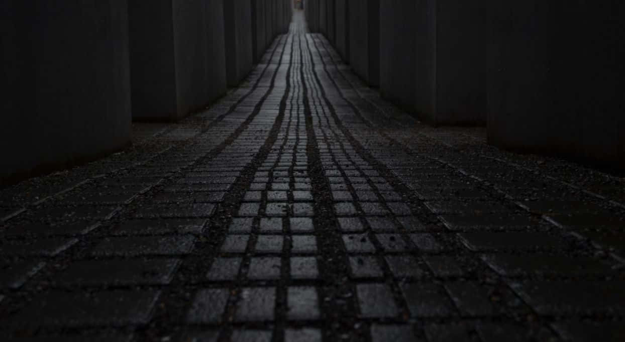 Dark Road 桌布 壁紙 — 一條狹窄濕滑的鵝卵石小路，在高大的灰色混凝土柱之間延伸向昏暗的遠方。