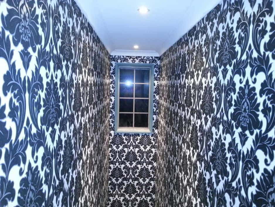 Installation Art 桌布 壁紙 — 一條狹窄的走廊，舖有華麗的黑白大馬士革牆紙，在明亮的吊燈下向著一扇小窗戶收窄。