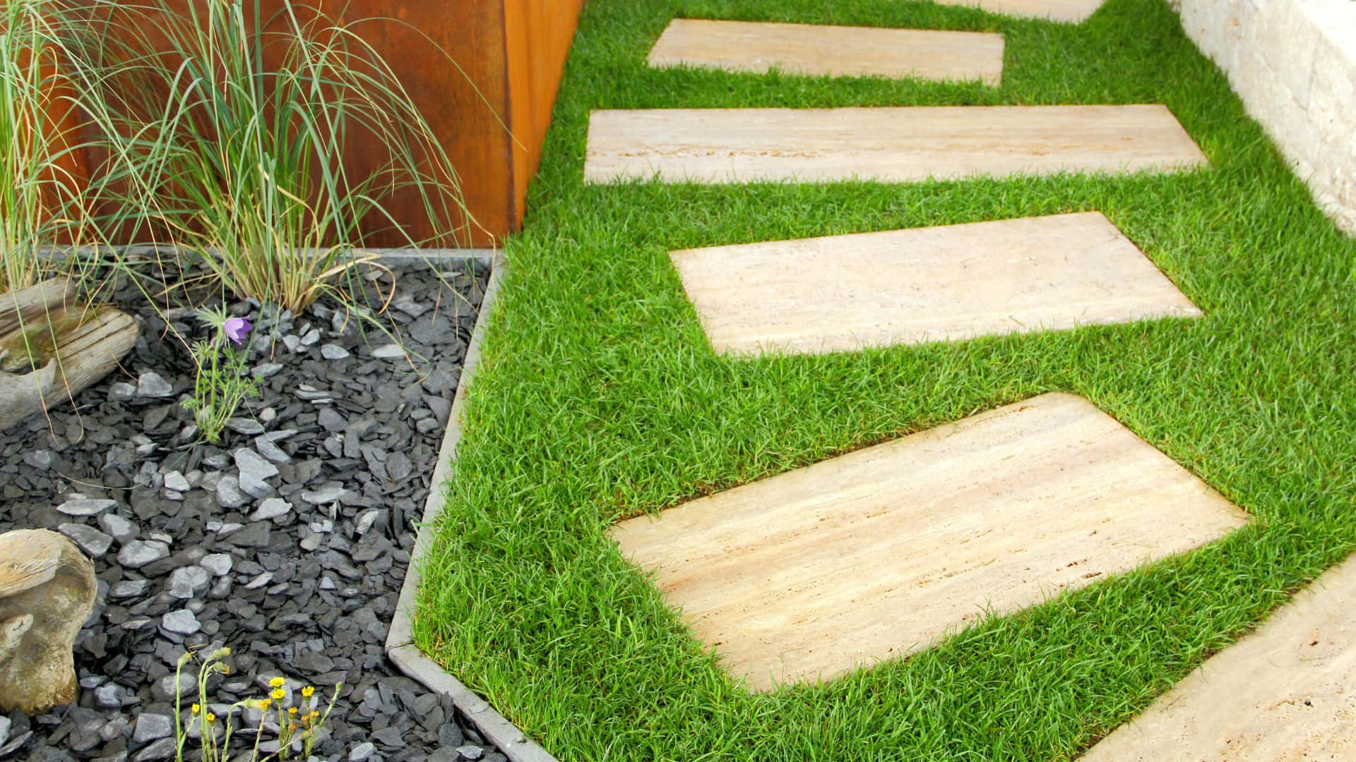 Garden Design 桌布 壁紙 — 一條由淺米色石板鋪成的蜿蜒小徑，穿過鮮綠的草地，旁邊是深灰色礫石床和高大的觀賞草。