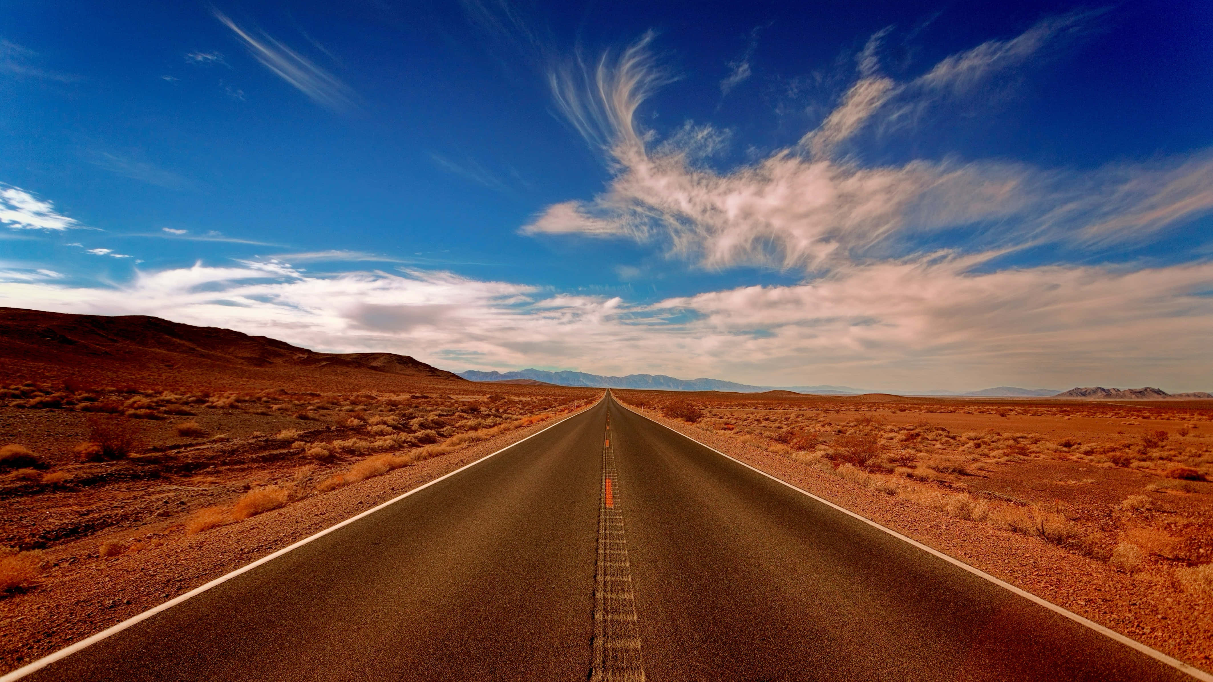 Journey 桌布 壁紙 — 一條筆直的瀝青公路穿過廣闊的沙漠，伸向遠方，上方是帶有縷縷白雲的湛藍天空。