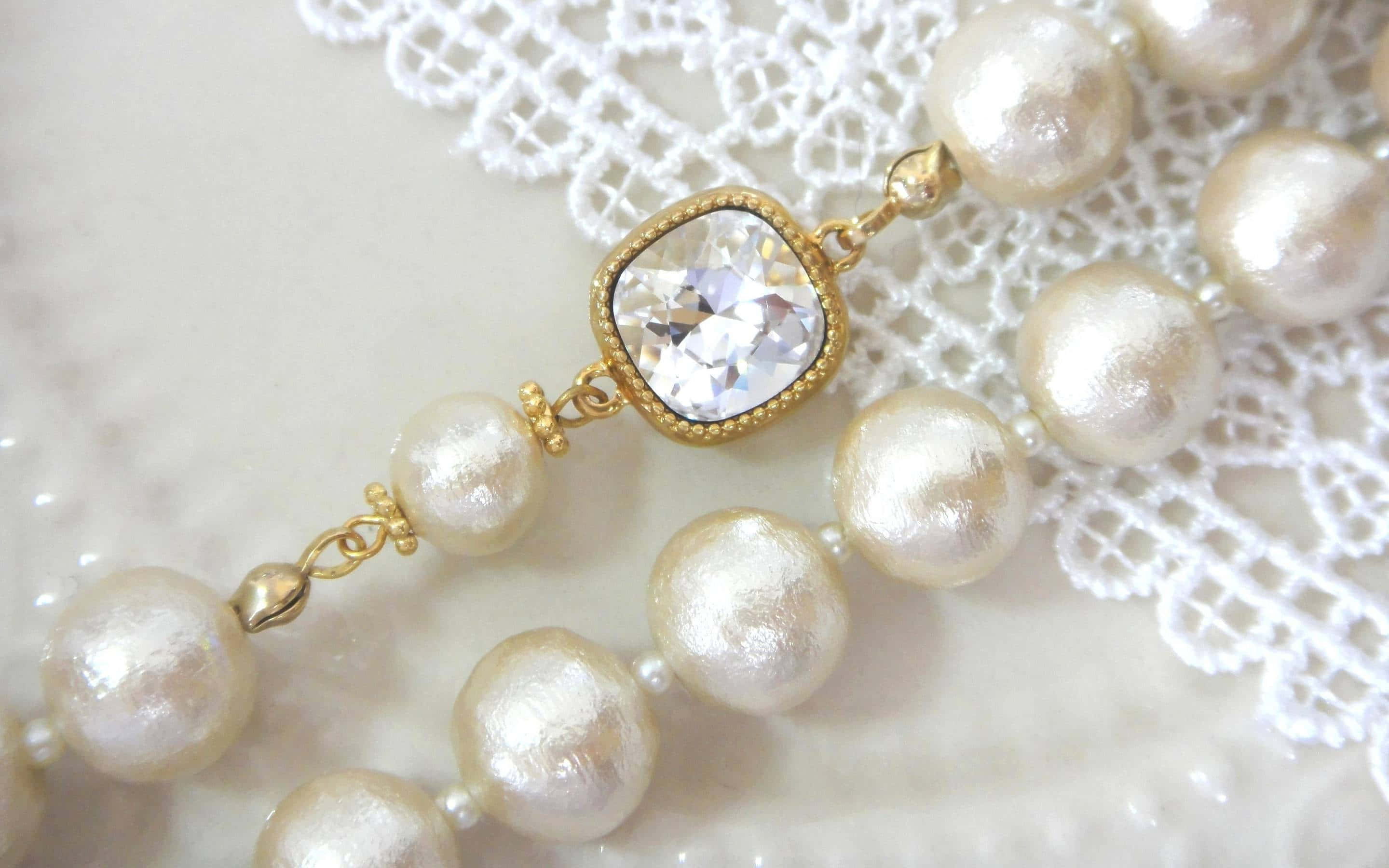 Jewelry Design 桌布 壁紙 — 一條精緻的珍珠項鍊，帶有金色水晶中心裝飾，優雅地躺在白色蕾絲上，背景是柔軟的大理石。