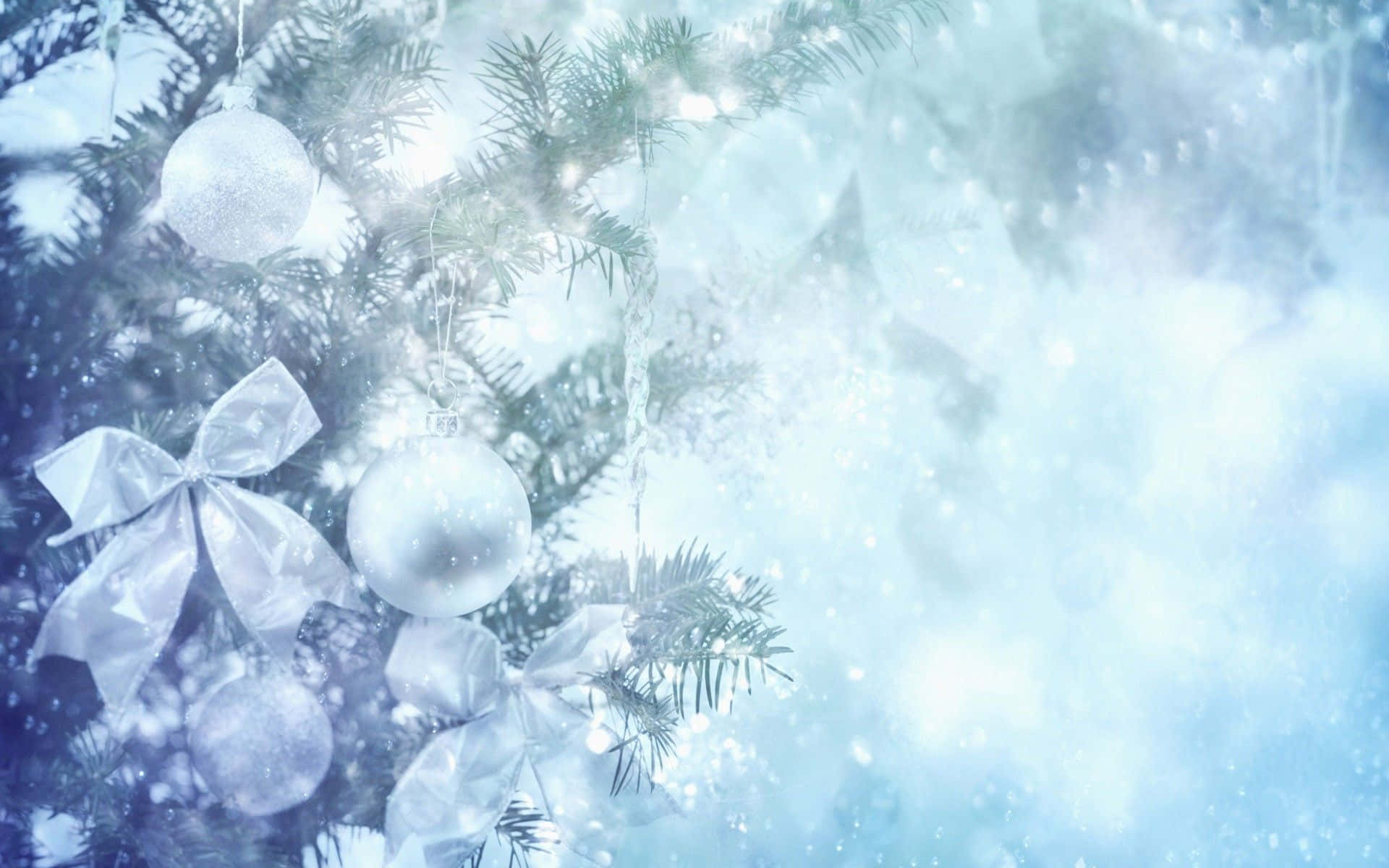 Winter Holiday 桌布 壁紙 — 一條結霜的常綠樹枝，飾有銀色裝飾品和蝴蝶結，在白雪皚皚、空靈的藍色背景下柔和地發光。