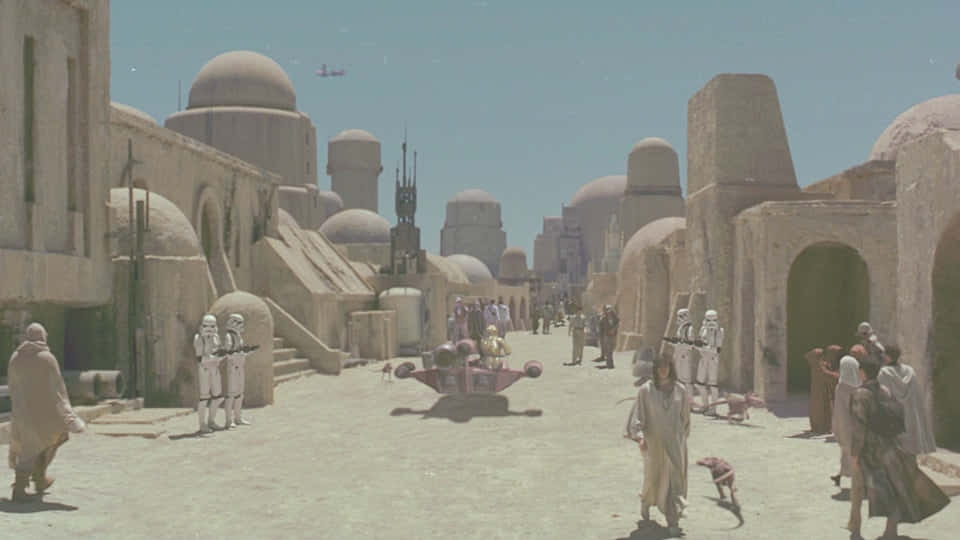 Mos Eisley 桌布 壁紙 — 一條繁忙的沙漠城市街道，有圓頂建築、風暴兵和飛行摩托車，在晴朗的藍天下。