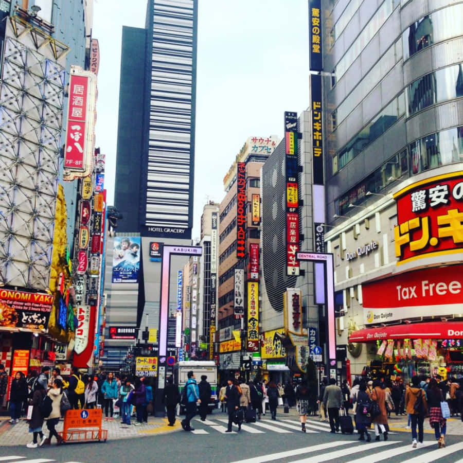 東京 桌布 壁紙 — 一條繁華的東京街道，充滿了高聳的建築物、霓虹燈招牌和穿越繁忙十字路口的人群。
