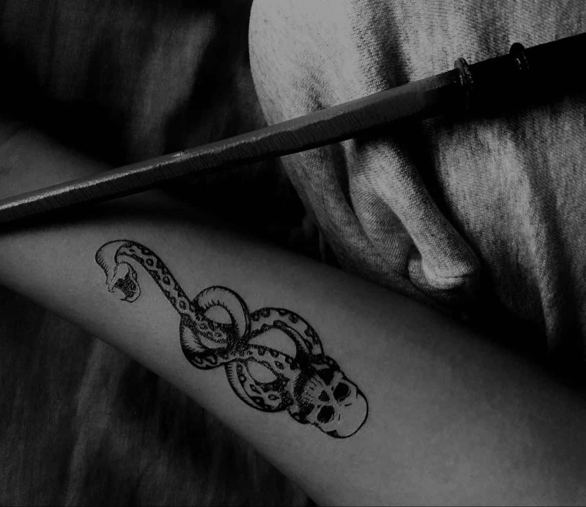 Death Eaters 桌布 壁紙 — 一條纏繞住骷髏頭嘅蛇紋身手臂黑白特寫，旁邊放住一把刀。