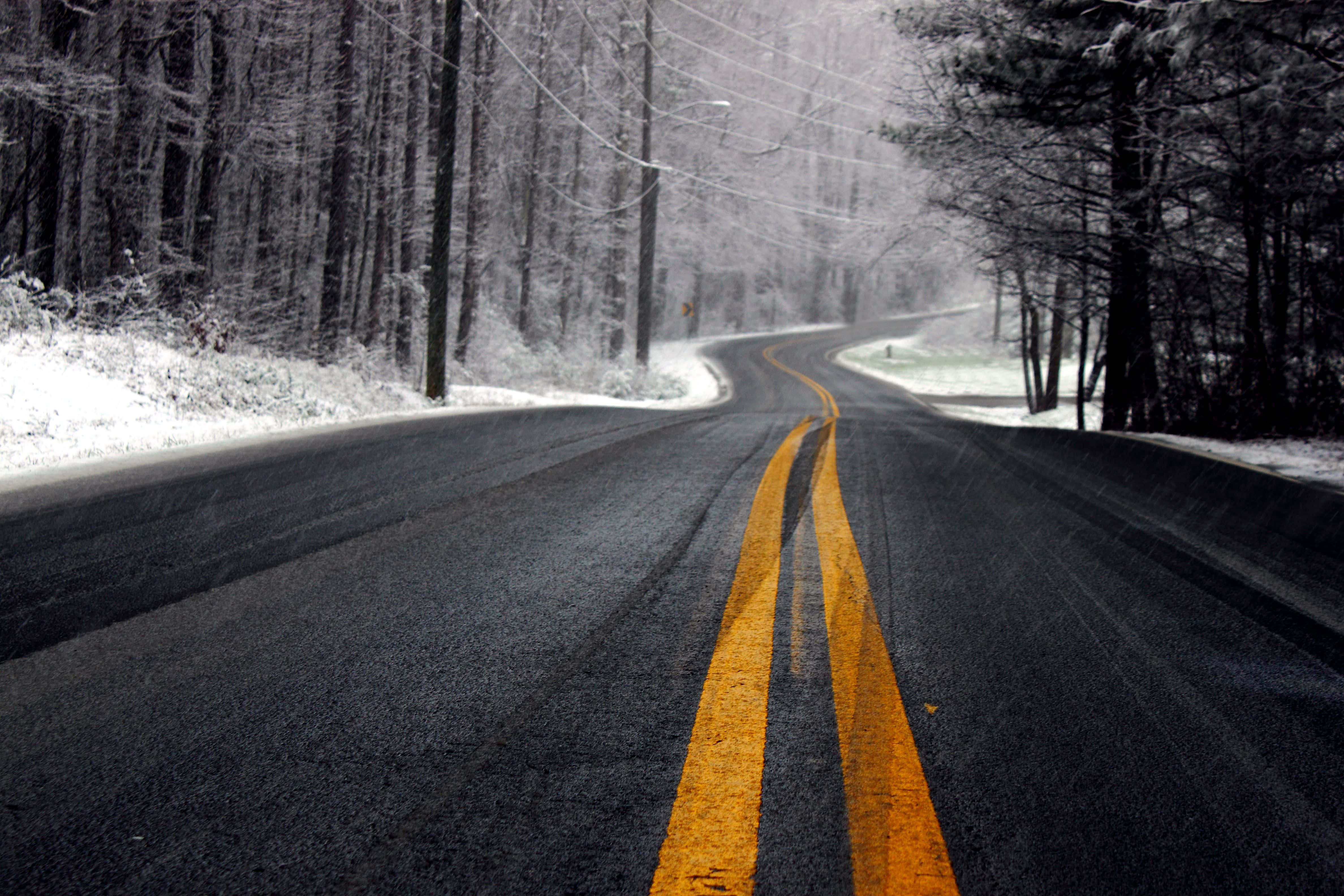 Icy Road 桌布 壁紙 — 一條蜿蜒的冬季道路穿過白雪覆蓋的森林，樹木光禿，明亮的黃色中心線清晰可見。