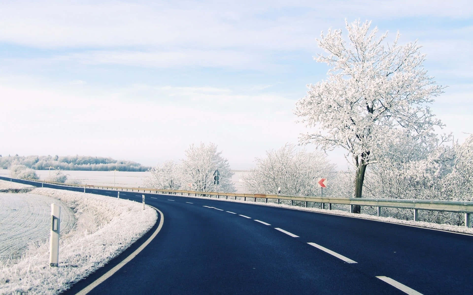 道路 桌布 壁紙 — 一條蜿蜒的瀝青路穿過結霜的冬季景觀，兩旁是白雪覆蓋的樹木和淡藍色的天空。