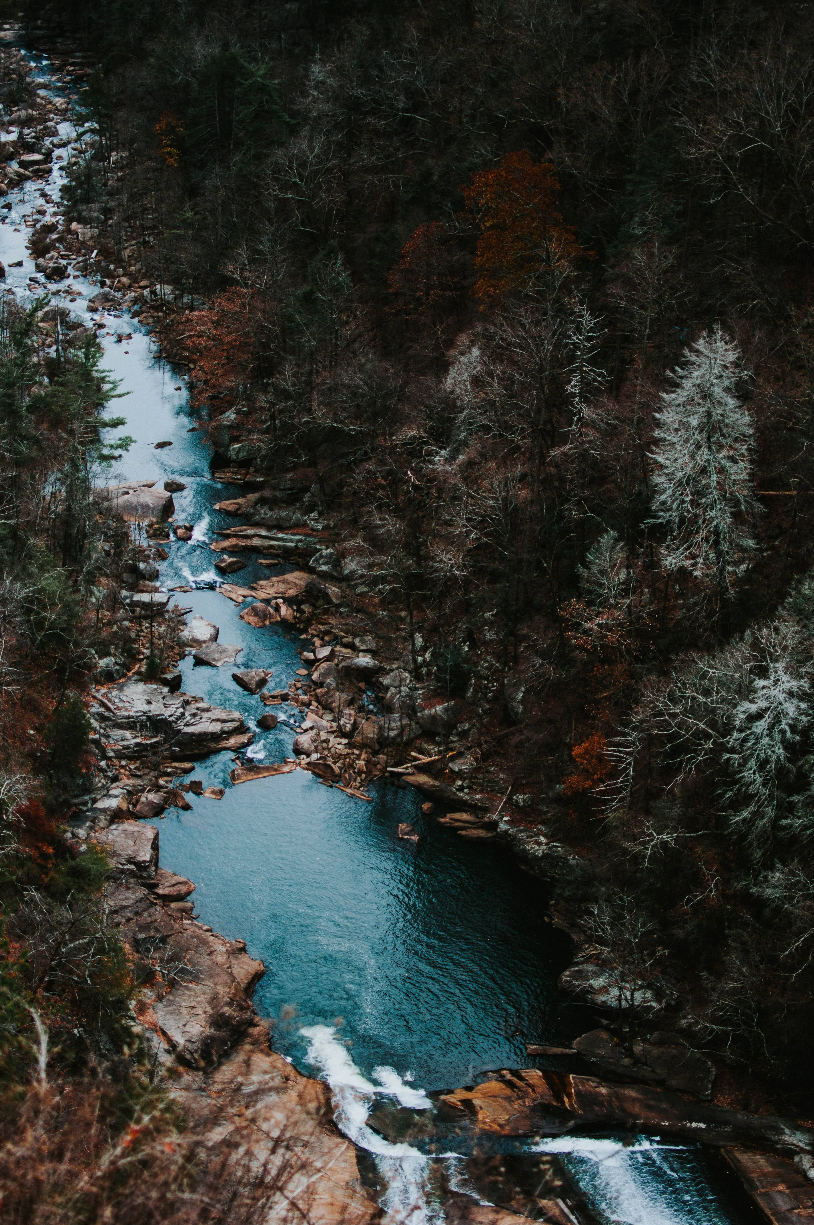 Tallulah Gorge iPhone 11 Pro Max 壁紙 — 一條蜿蜒的藍綠色河流穿過茂密的森林，樹木光禿，岩石河岸上點綴著積雪。