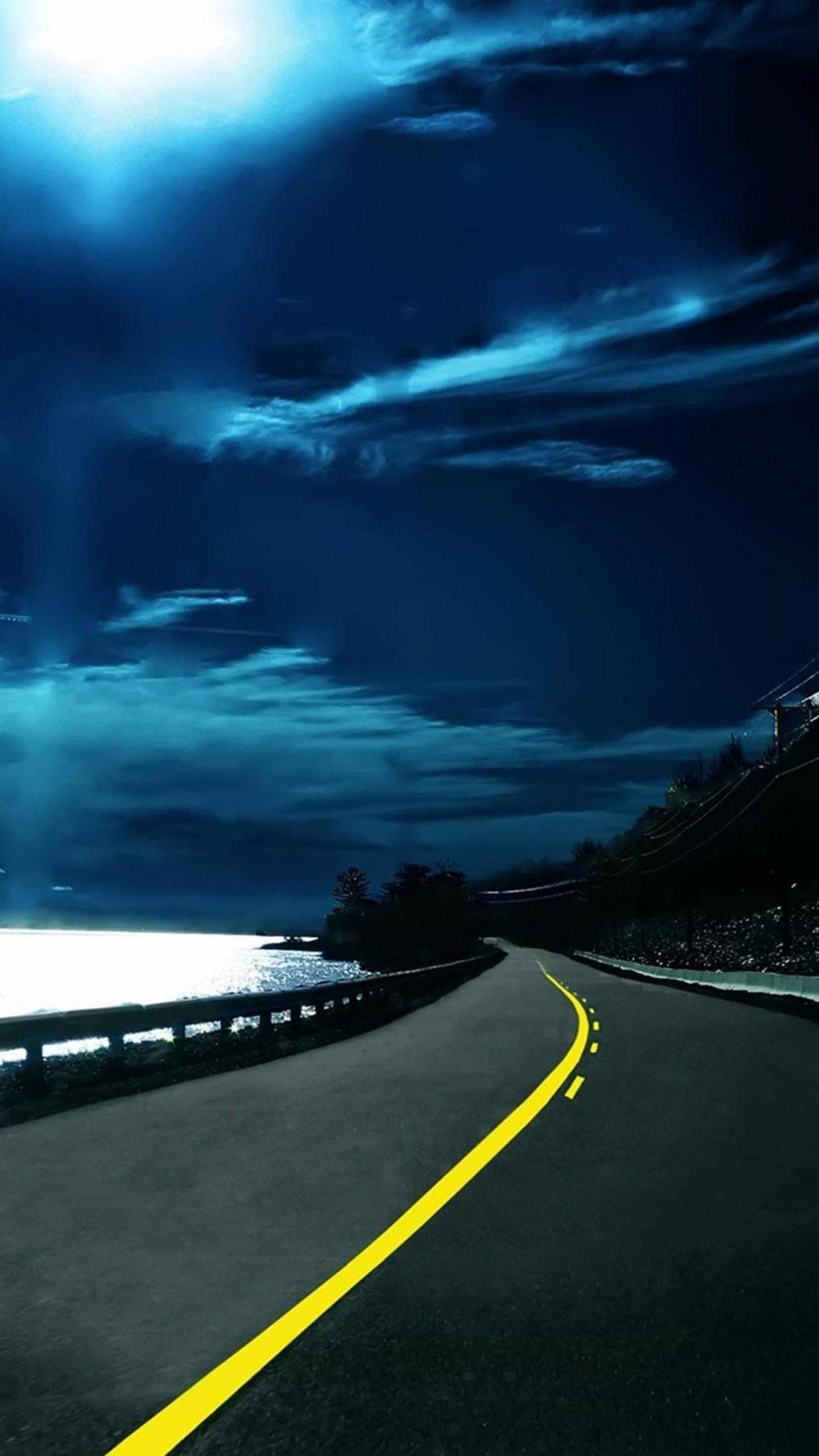夜空 桌布 壁紙 — 一條蜿蜒的道路在戲劇性的藍色夜空和條紋雲下彎向發光的地平線。
