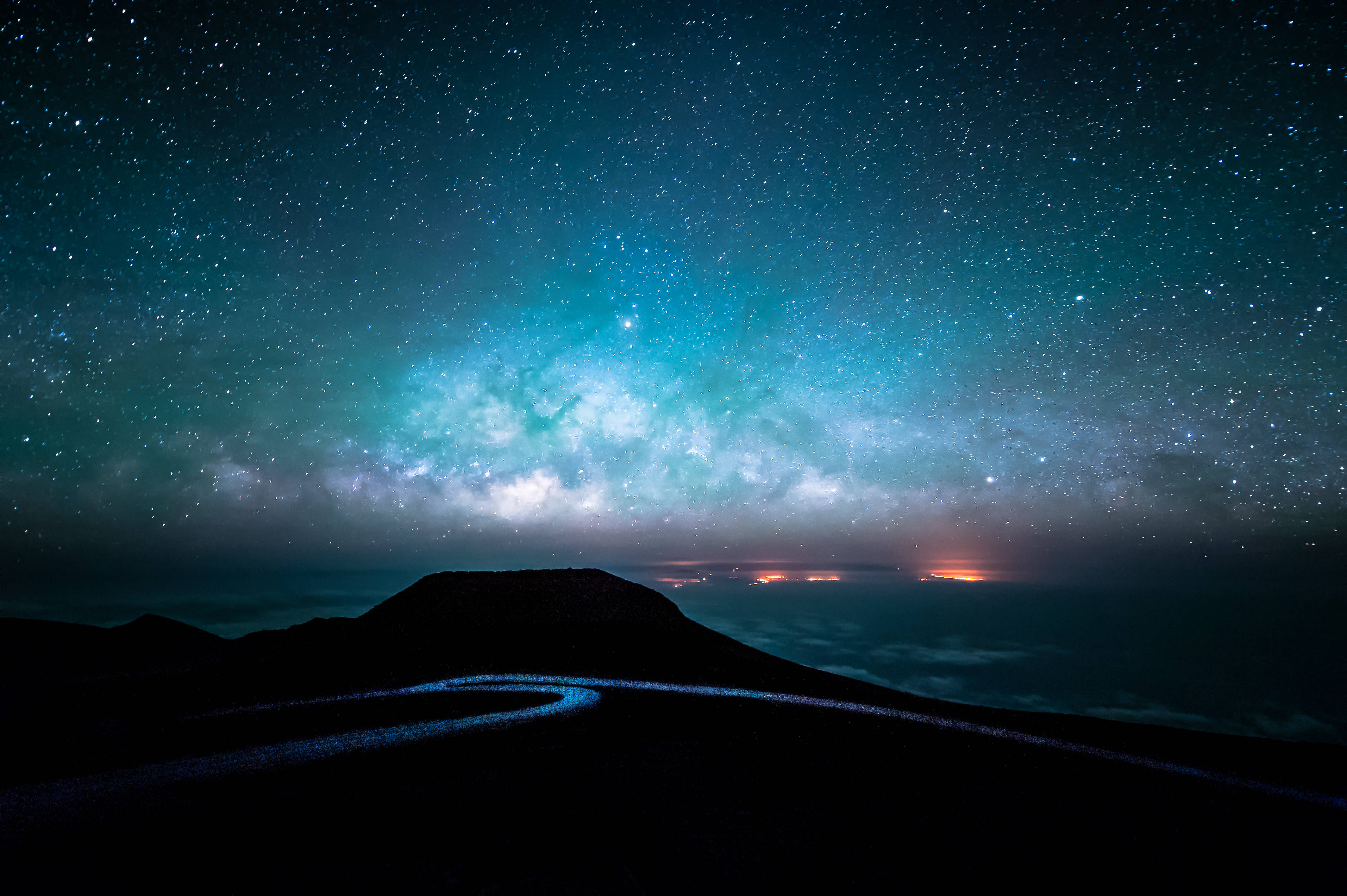 星空 桌布 壁紙 — 一條蜿蜒的道路在黑暗的山脈中穿行，上方是充滿活力的藍綠色星空，閃耀的銀河發出光芒。