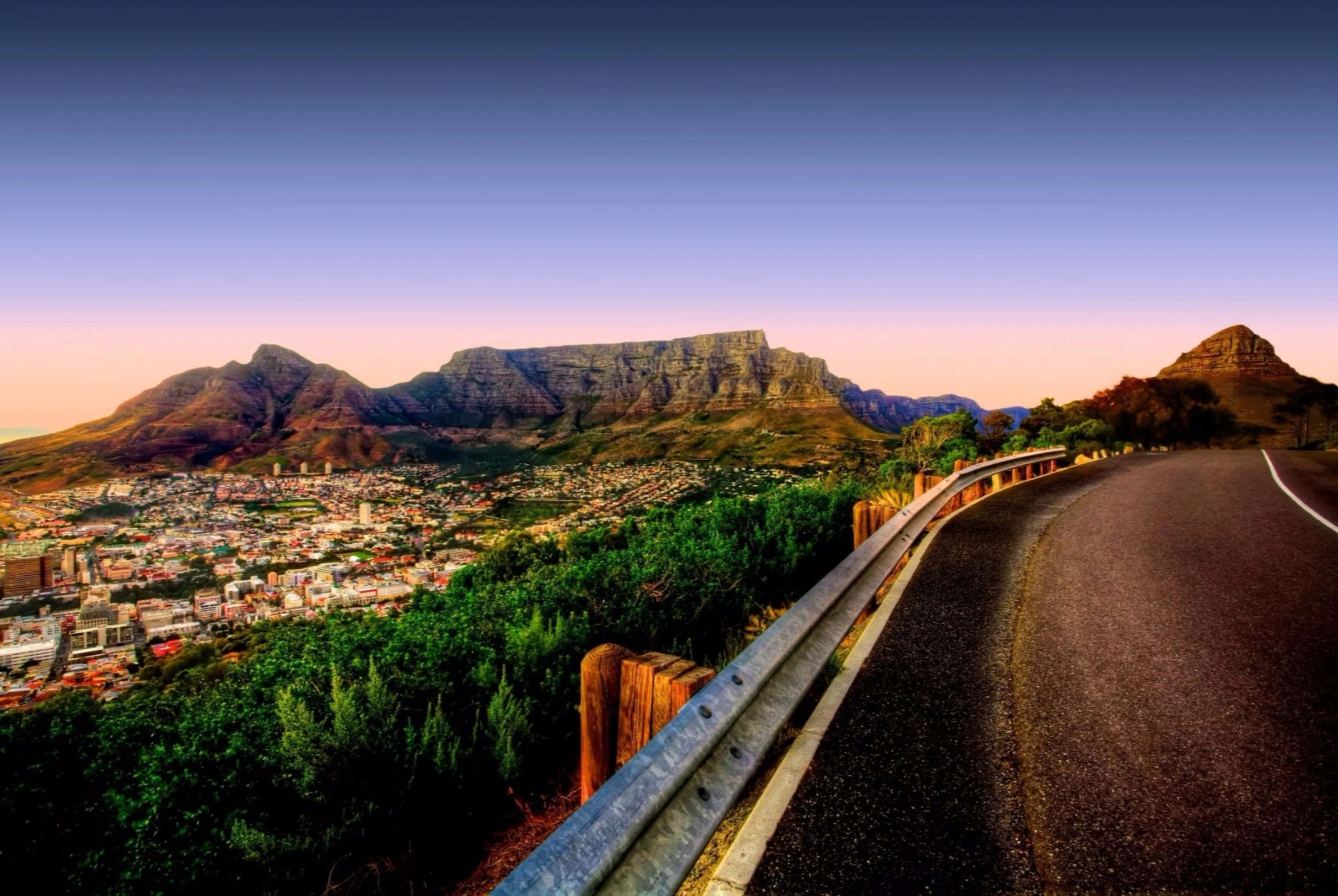 South Africa 桌布 壁紙 — 一條蜿蜒的道路沿著懸崖蜿蜒而行，俯瞰著日落時分雄偉的桌山腳下蔓延的城市。