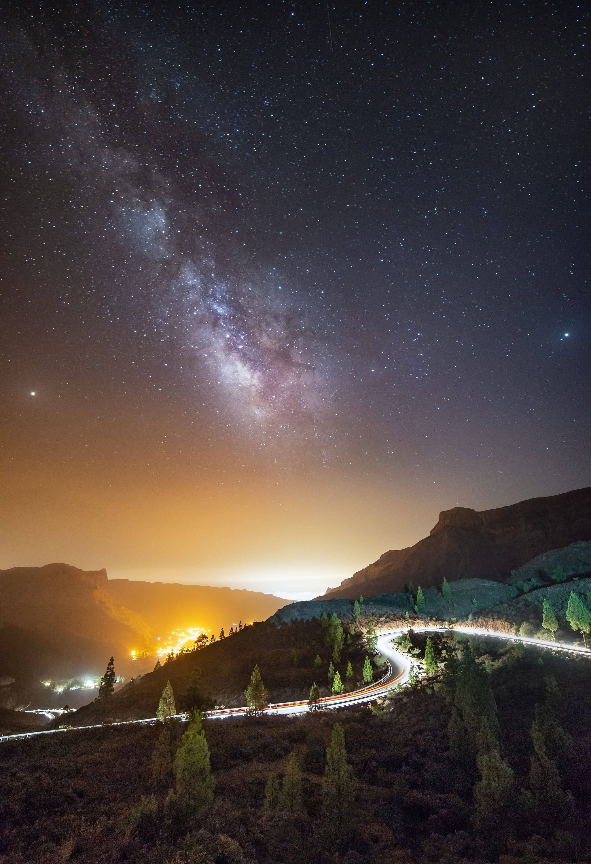 道路 桌布 壁紙 — 一條蜿蜒的道路穿過山區景觀，上方是充滿活力的星空，銀河在頭頂閃耀。